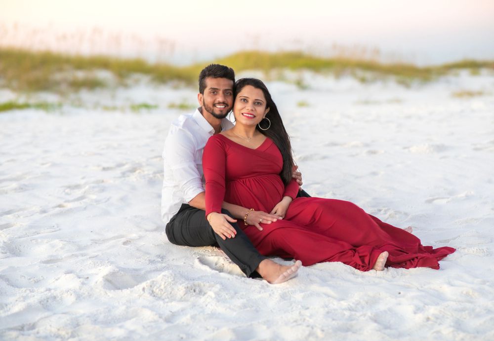 A romantic couple in formal attire sits together on pristine white sand beach during sunset.