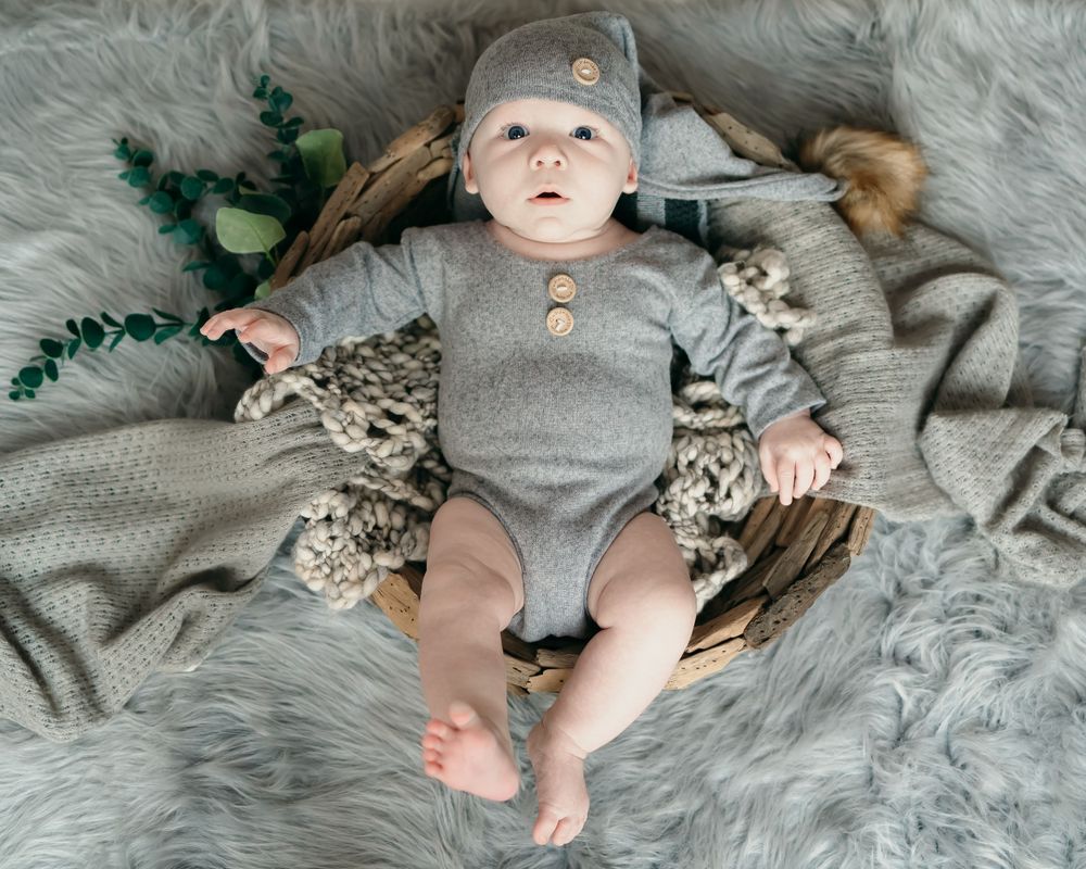 Baby in gray outfit lies on fur blanket with greenery accents.