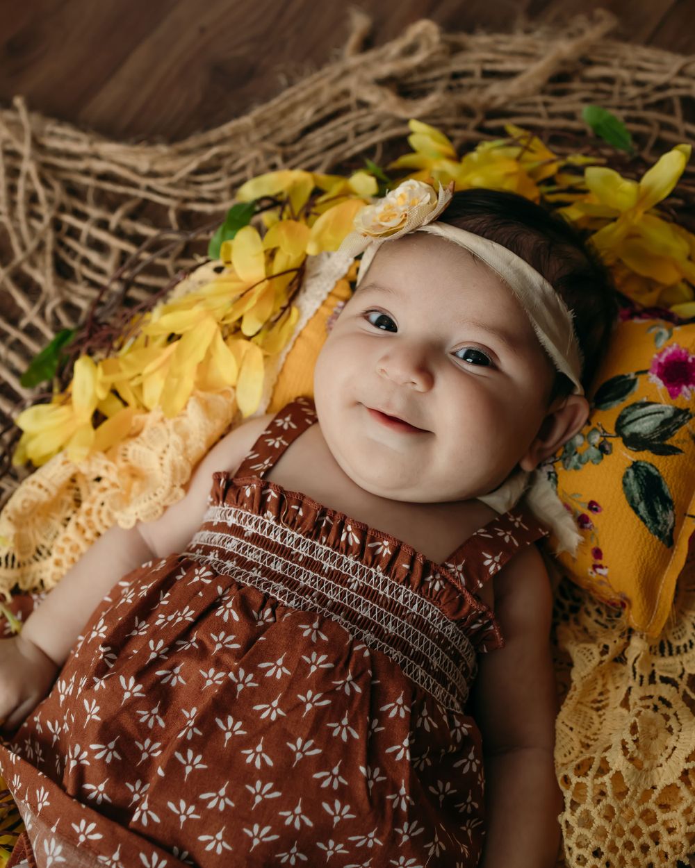 Close up of baby in floral dress surrounded by yellow flowers and lace.