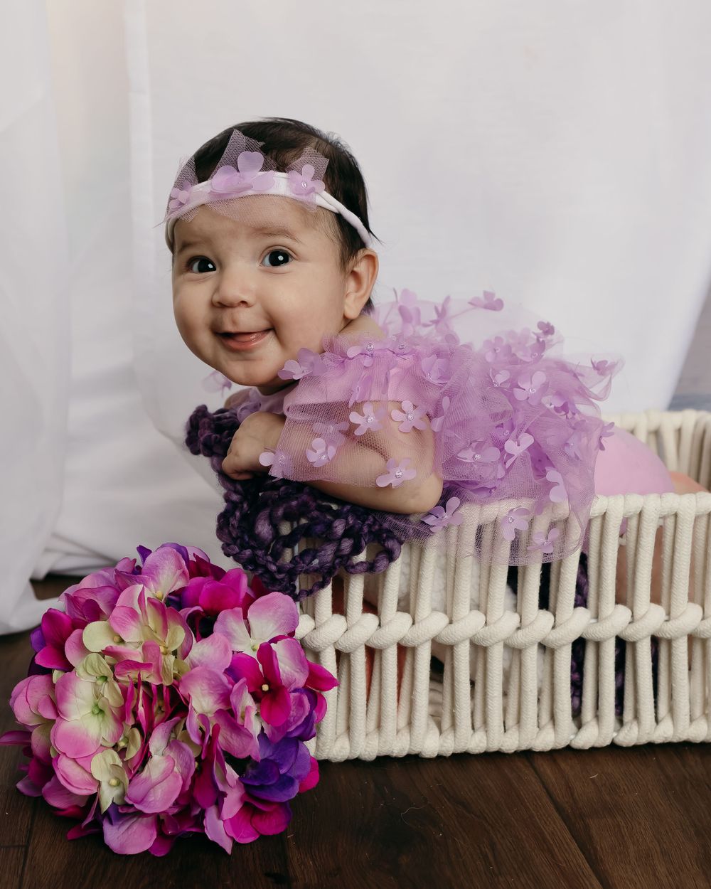 Baby in purple tulle dress posed with pink hydrangeas and white wicker. Milestone sessions owatonna Mn