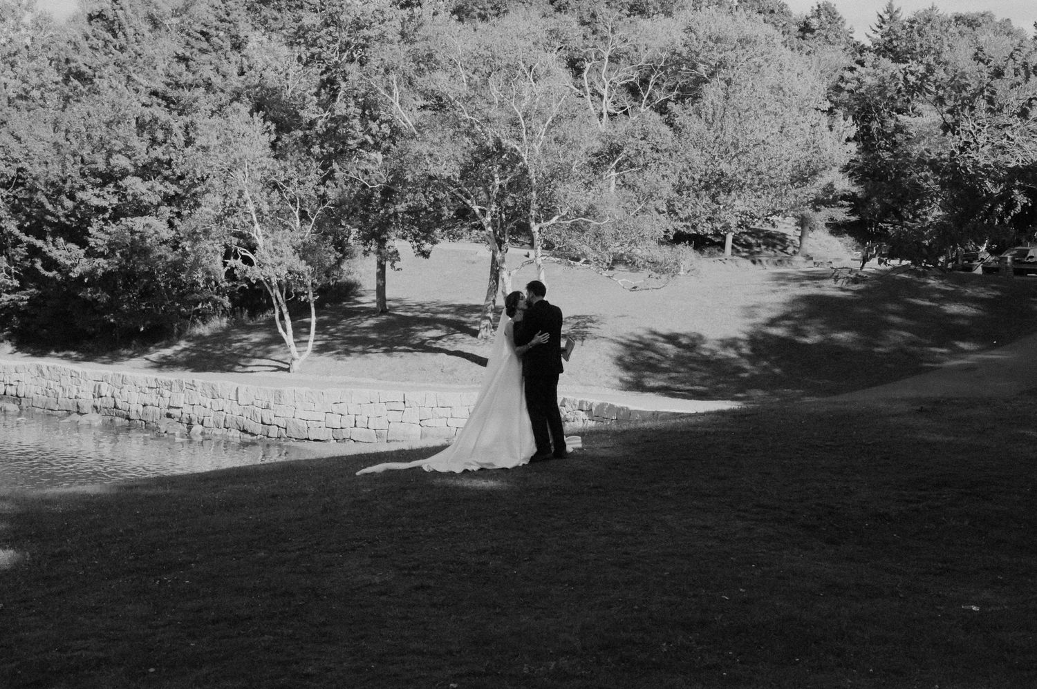 Black and white landscape shot of newlyweds embracing on grassy hillside.