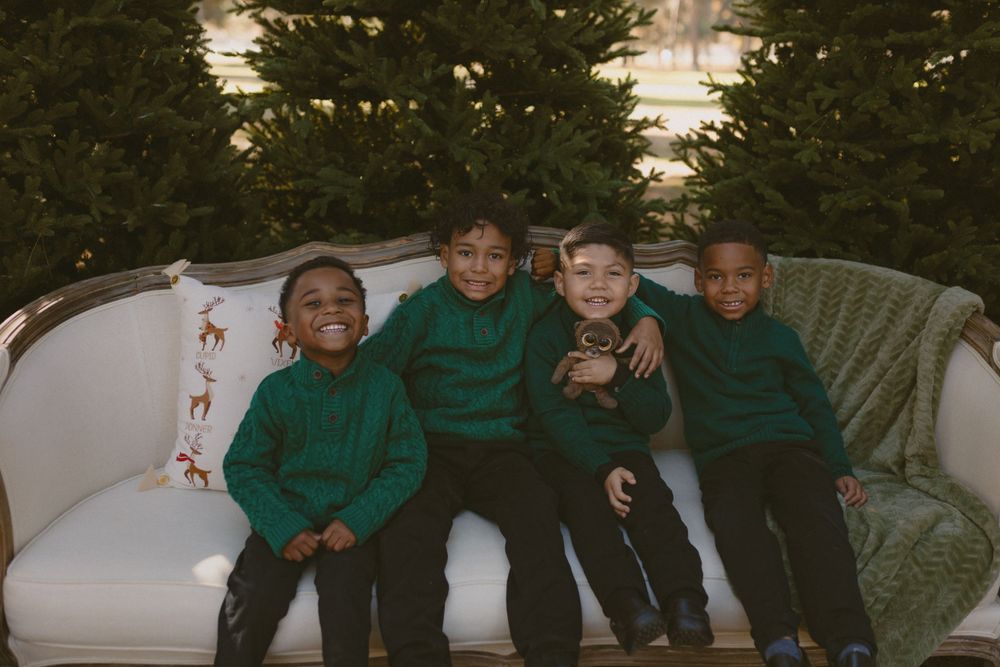 Four children sitting together on a white wicker sofa wearing matching green shirts.