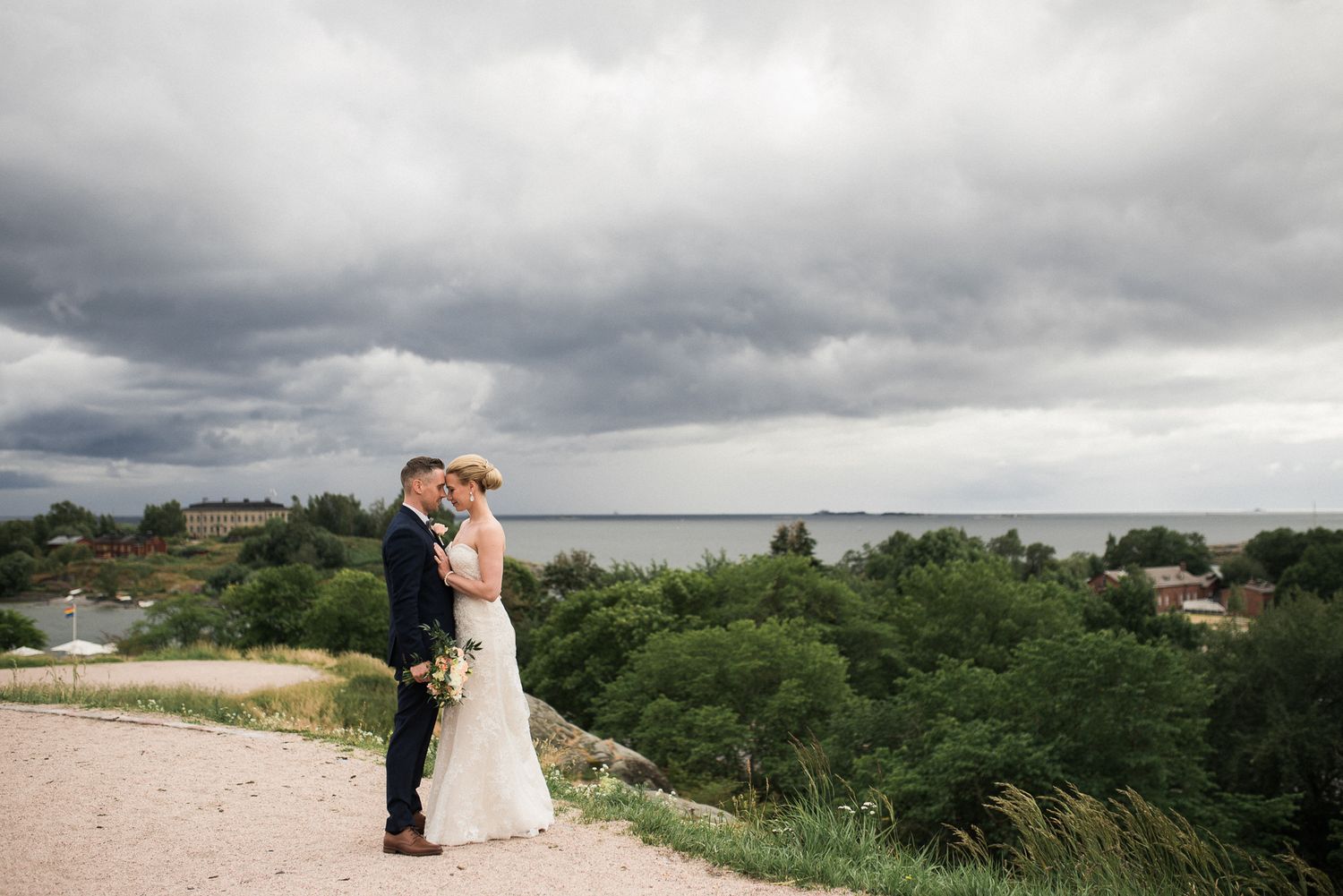 A couple shares a romantic moment on a hilltop overlooking a coastal landscape under dramatic storm clouds.