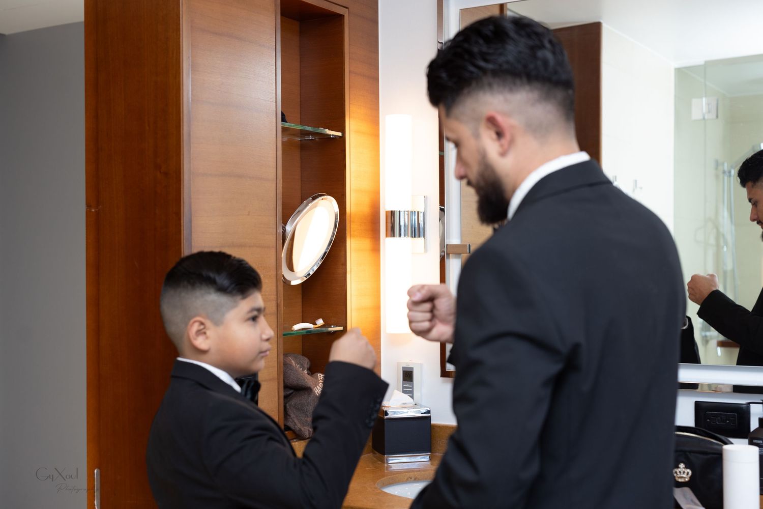 A formal dress preparation scene with matching black suits in a well-lit room.