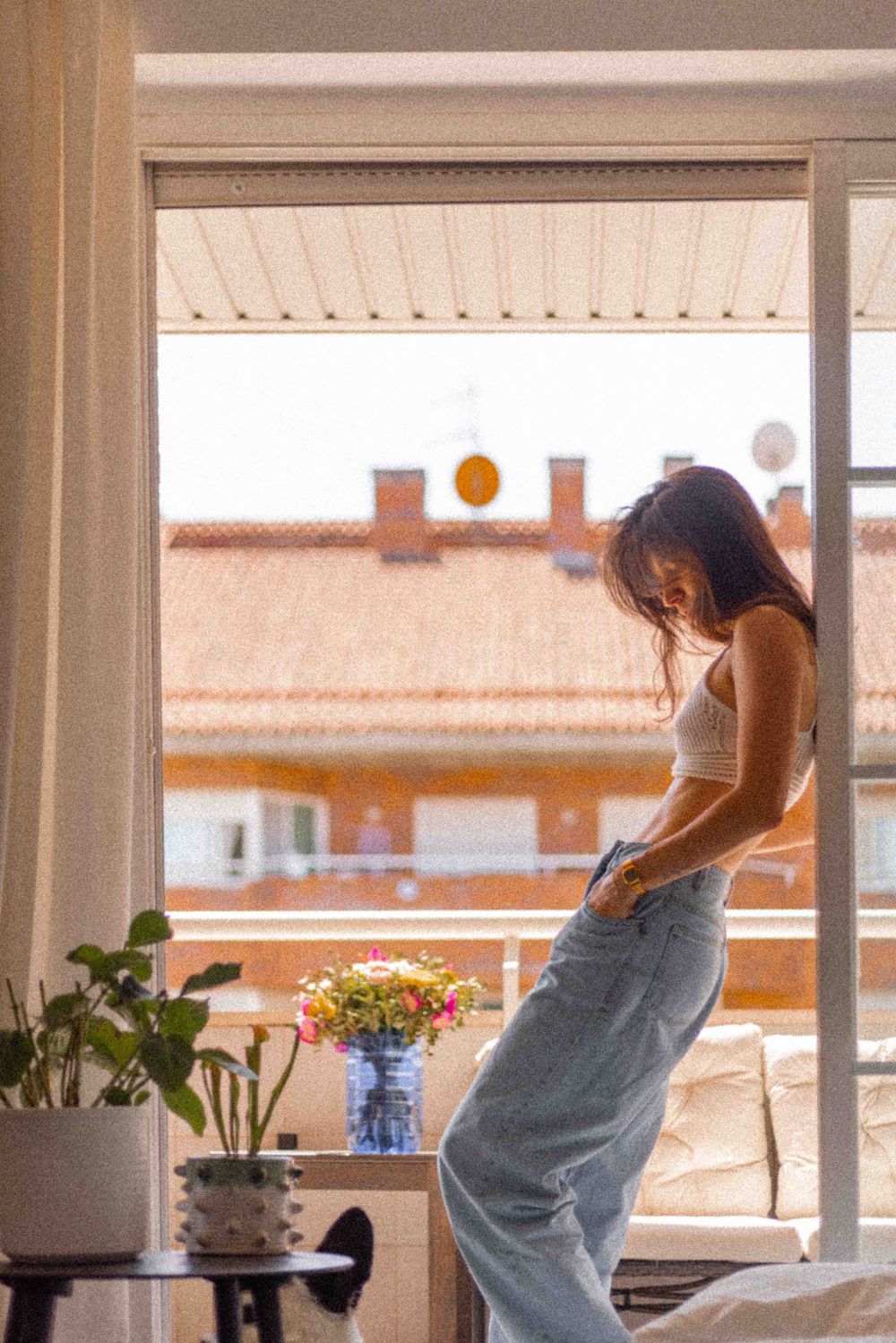 Bright window view with potted plants and flowers on windowsill as figure dances in casual jeans and crop top outfit.