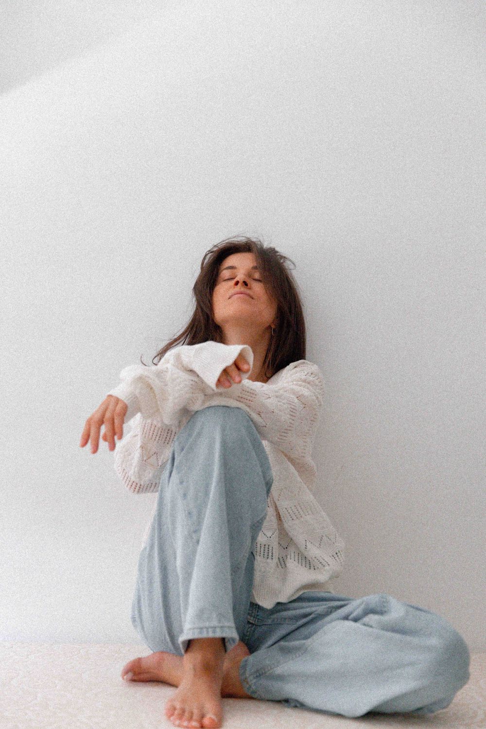 Minimalist portrait against white wall wearing cozy white sweater and denim.
