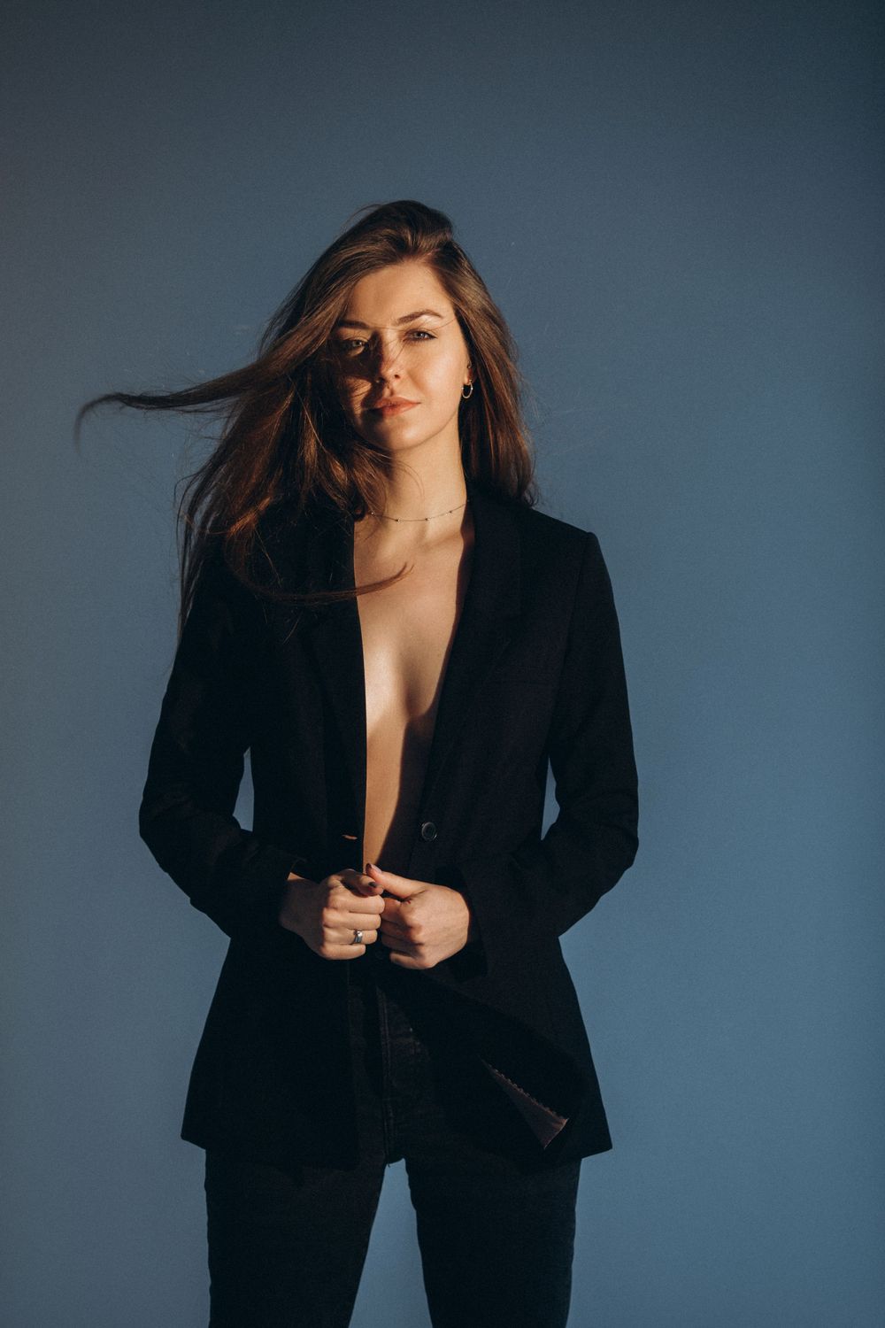 Fashion portrait with someone in black blazer against blue backdrop with windswept hair.