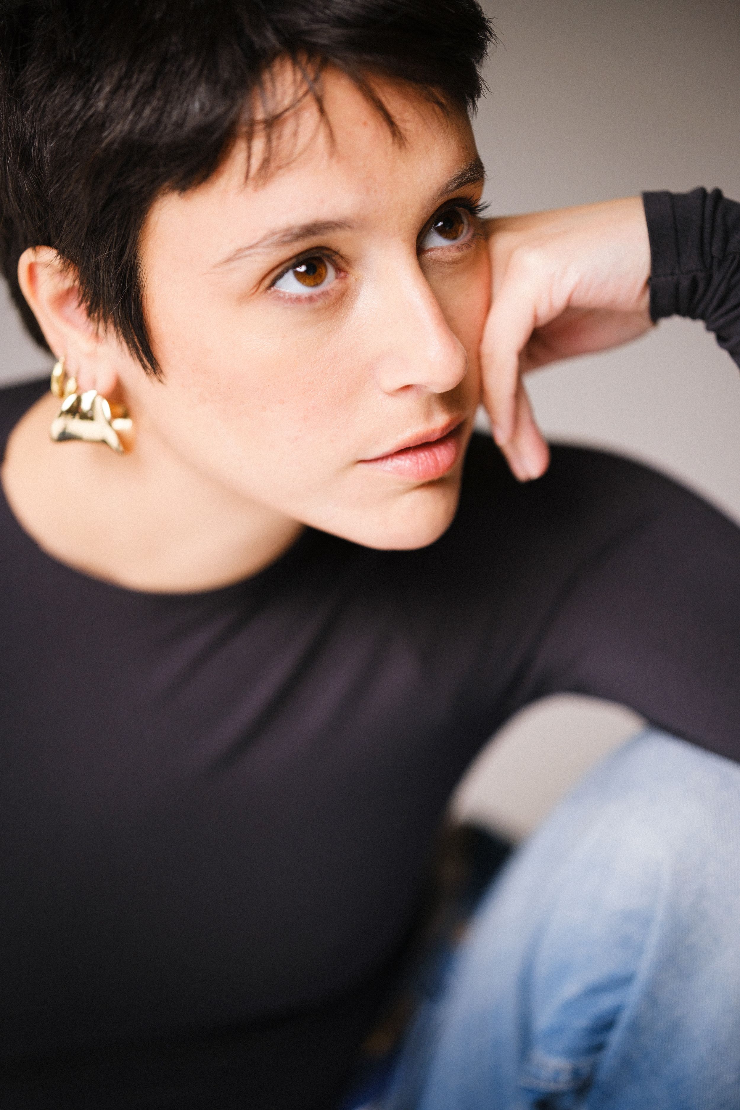 Dramatic studio portrait featuring black turtleneck and gold earring against grey backdrop.