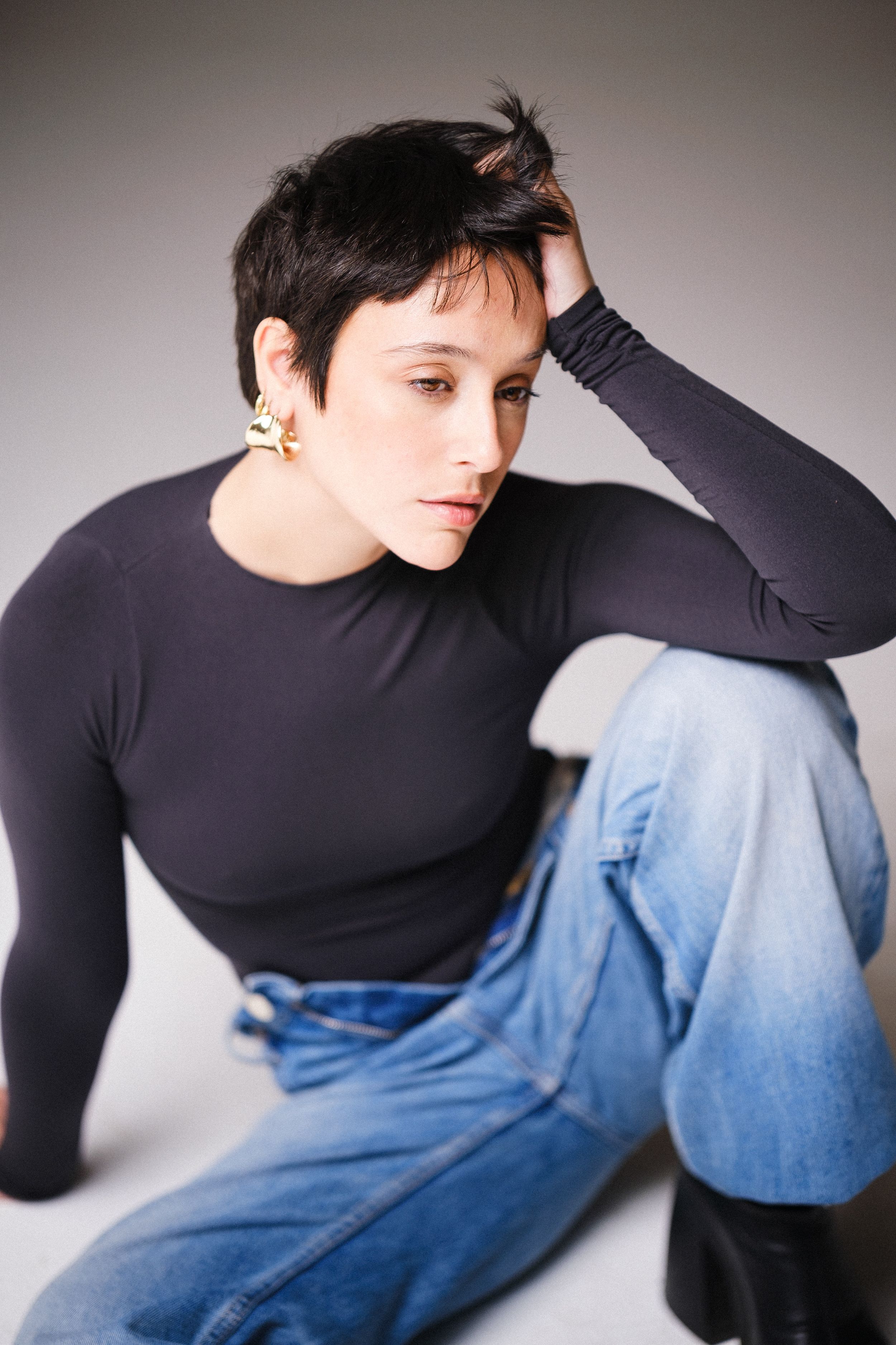 Fashion portrait with relaxed poses in black turtleneck and denim against grey backdrop.