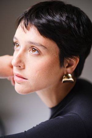 Side profile portrait with delicate gold jewelry and short dark hair.