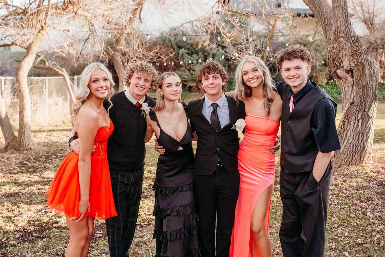 Group photo of friends in formal attire including red and black dresses at an outdoor event.