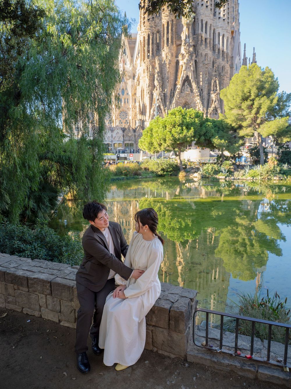 A couple shares a romantic moment by a reflecting pond near the Sagrada Familia cathedral.