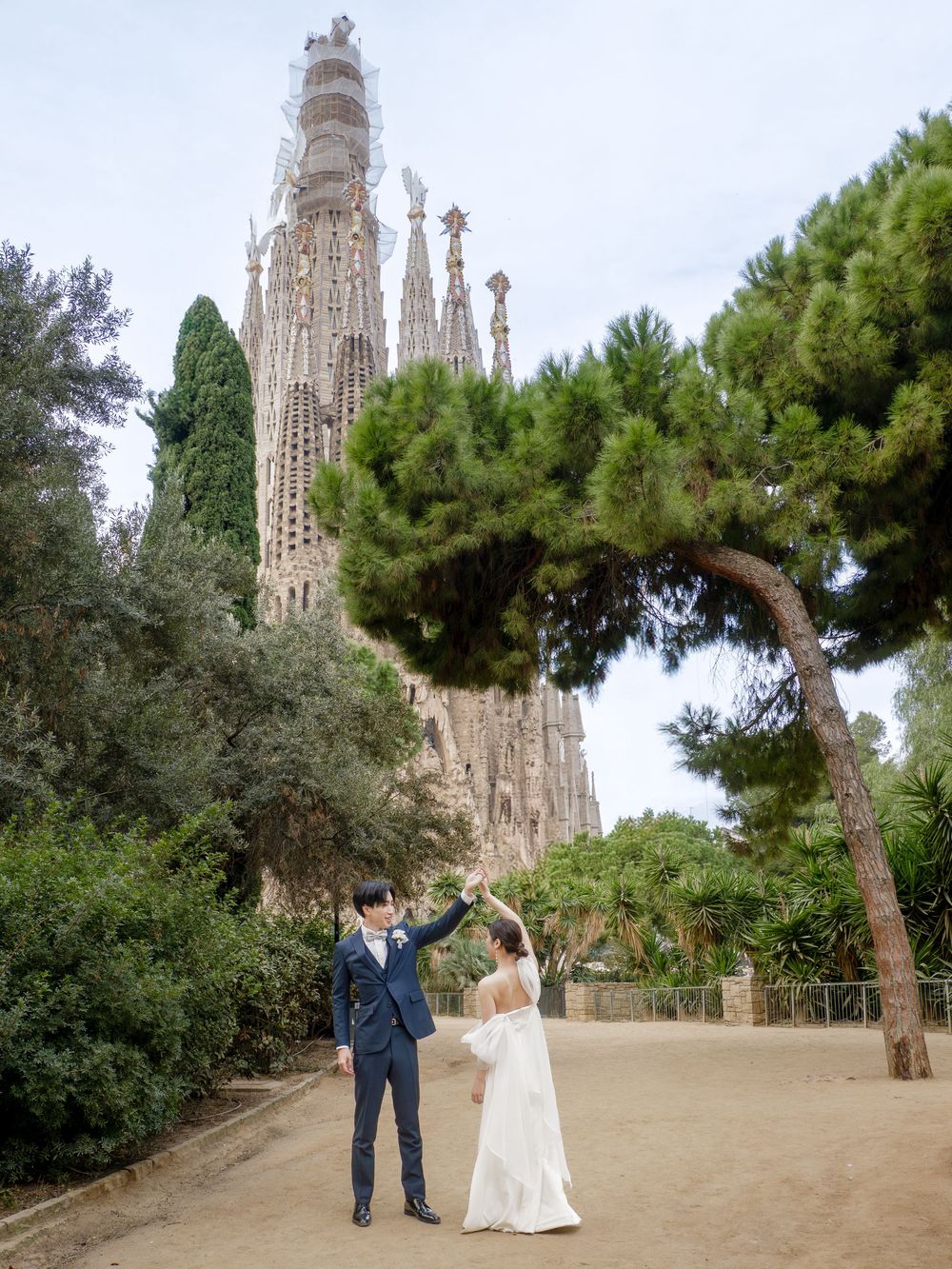 Post wedding photos being taken in a park with the majestic Sagrada Familia towers visible in the background.