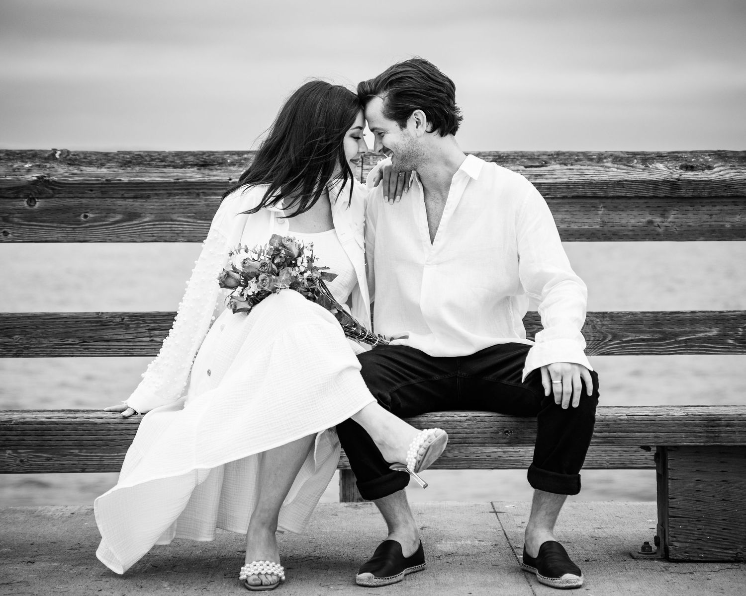 Black and white engagement photo of a smilin laughing together while holding hands on a pier, captured by Chris Cornish Photography.