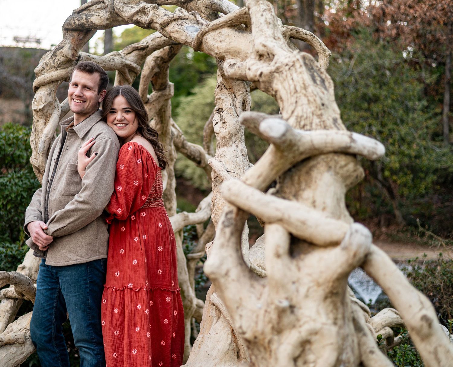 Happy couple embracing among twisted tree sculptures in a romantic garden setting.