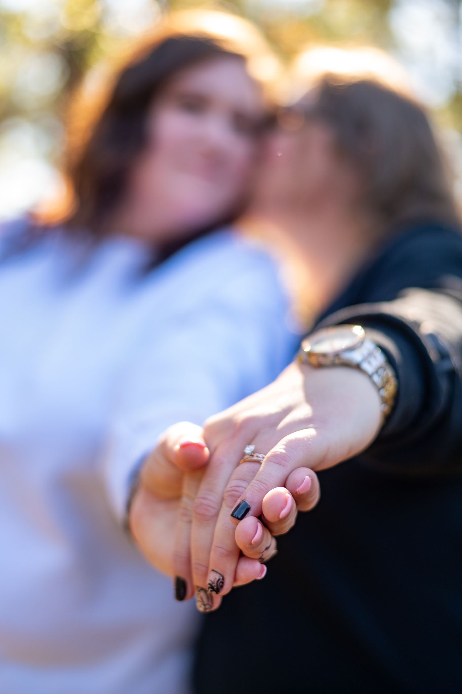 Close-up of couple holding hands showing engagement ring in soft bokeh light.