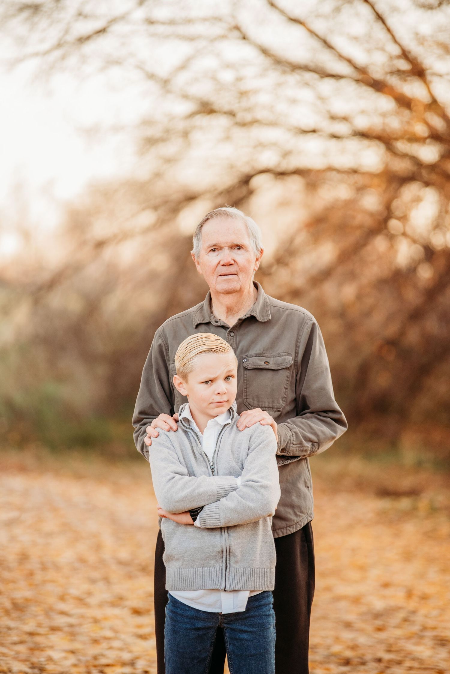 An outdoor family portrait with autumn trees and golden sunlight in the background.