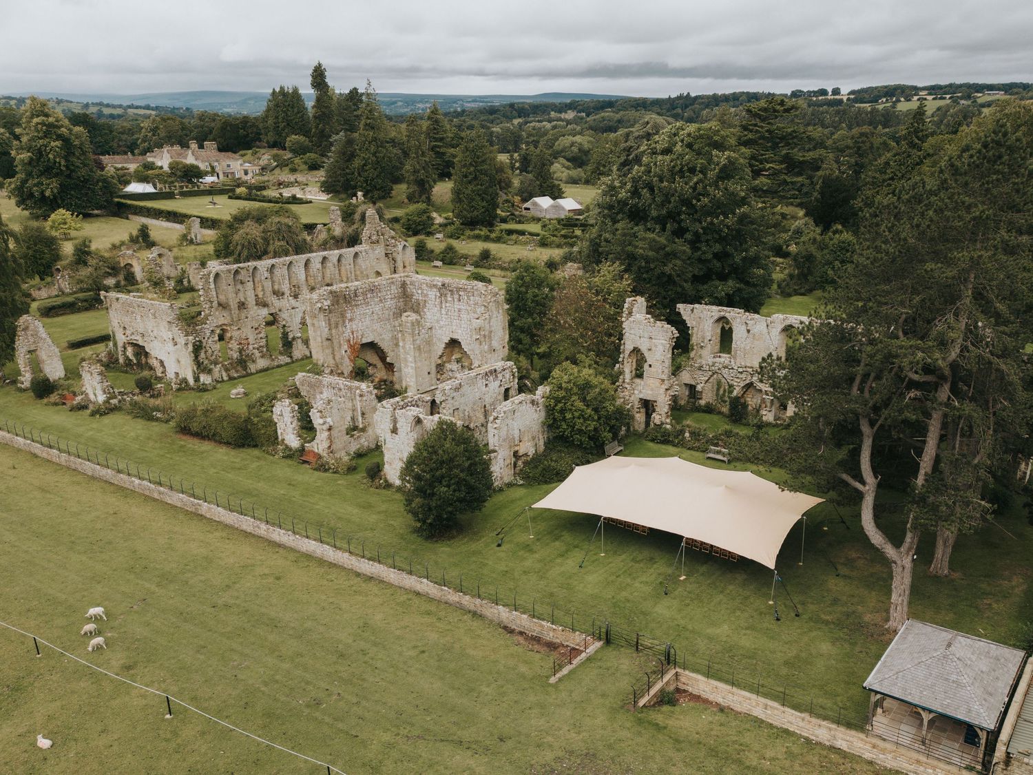 Aerial view of historic stone abbey ruins with a white canopy tent on manicured grounds in the English countryside.
