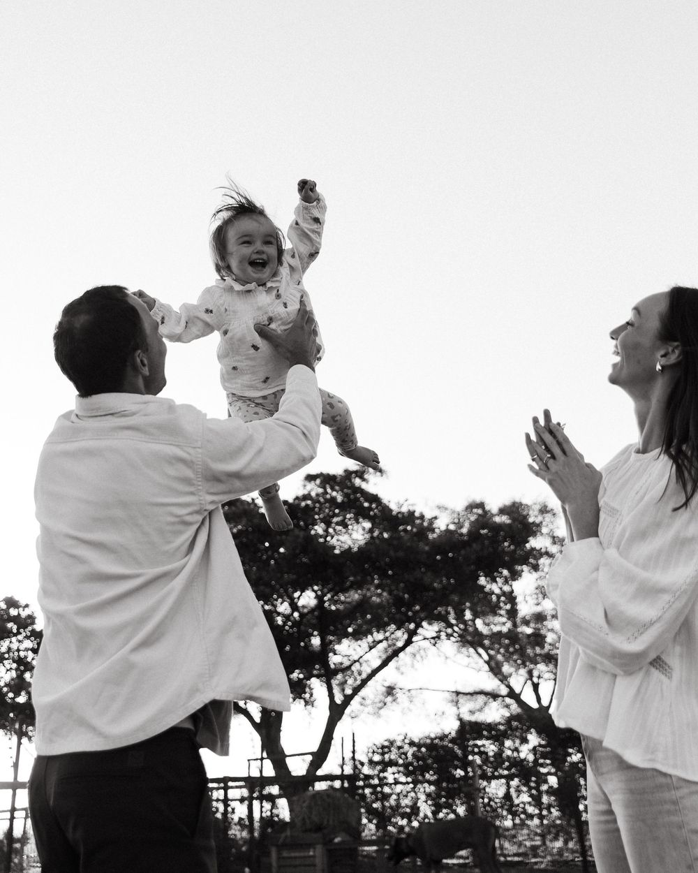 A joyful family moment captured in black and white as a small child is lifted high in the air.