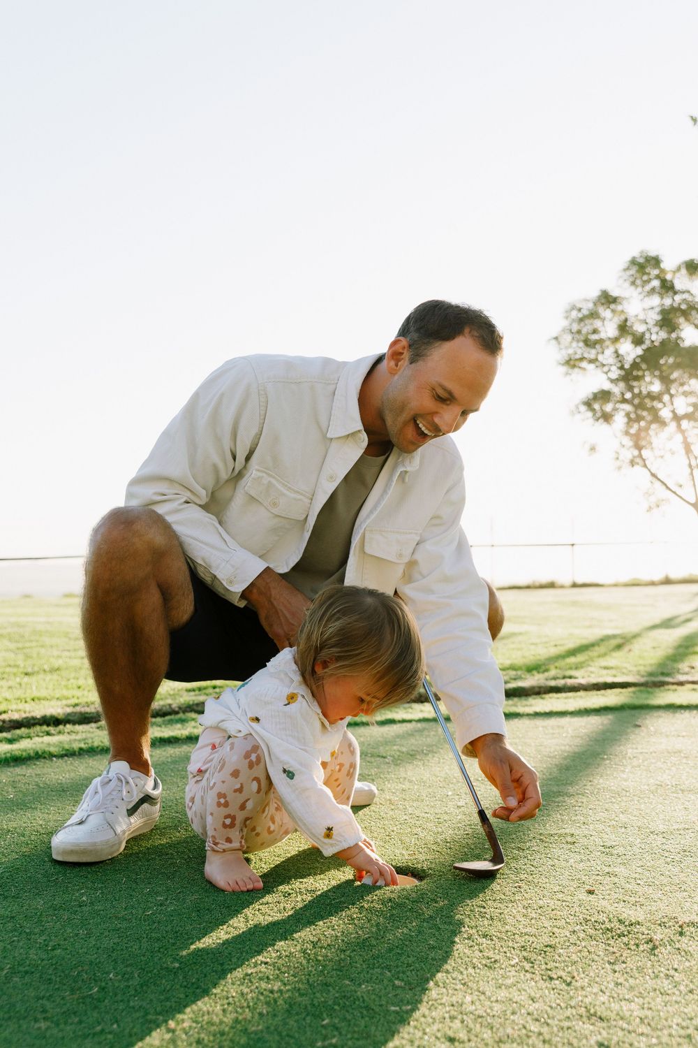 Caregiver and small child explore together on grassy field during golden hour sunlight.