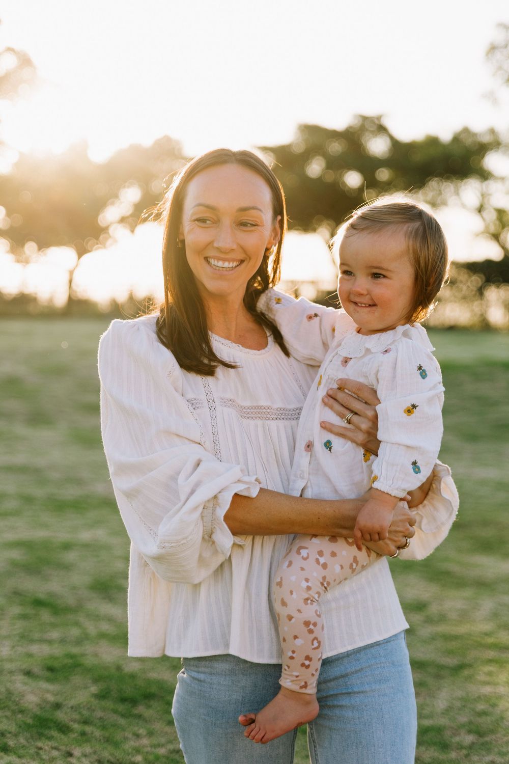 A tender moment captured at golden hour showing a parent and child embracing outdoors in white outfits.