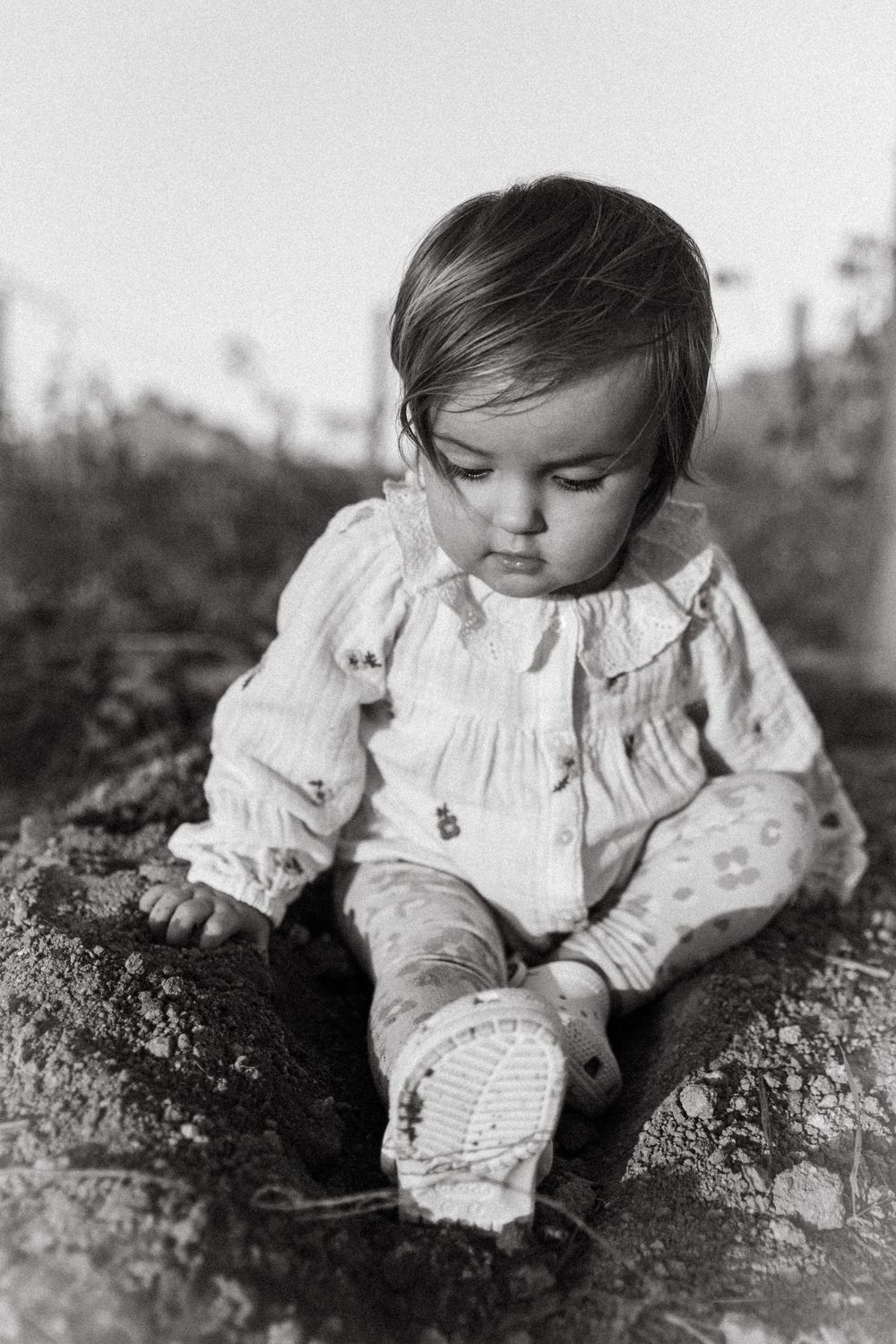 Black and white series of photos showing a small child in a white dress lying on the ground.