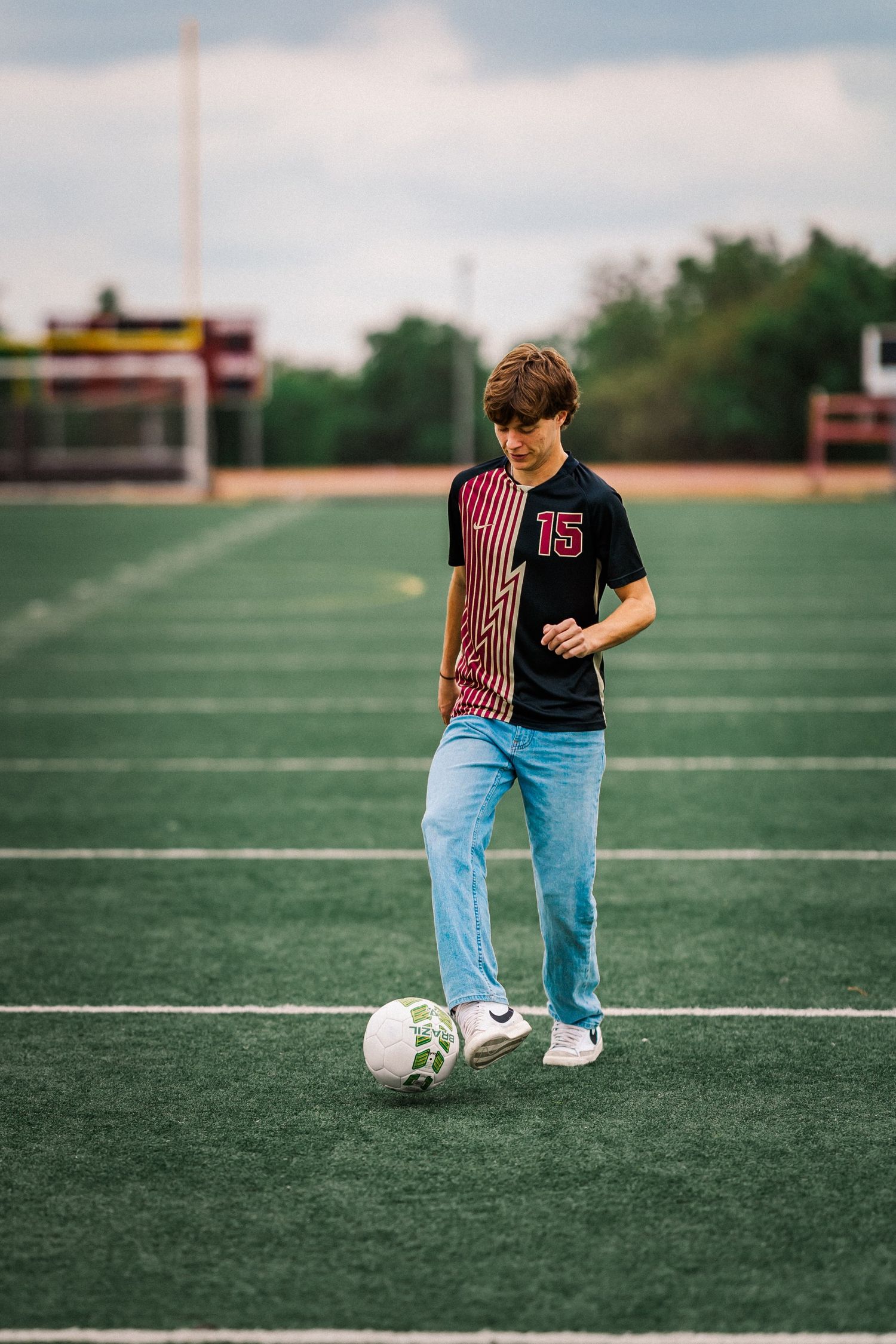 Teen boy in number 15 soccer jersey dribbling ball on turf field for senior sports portrait.