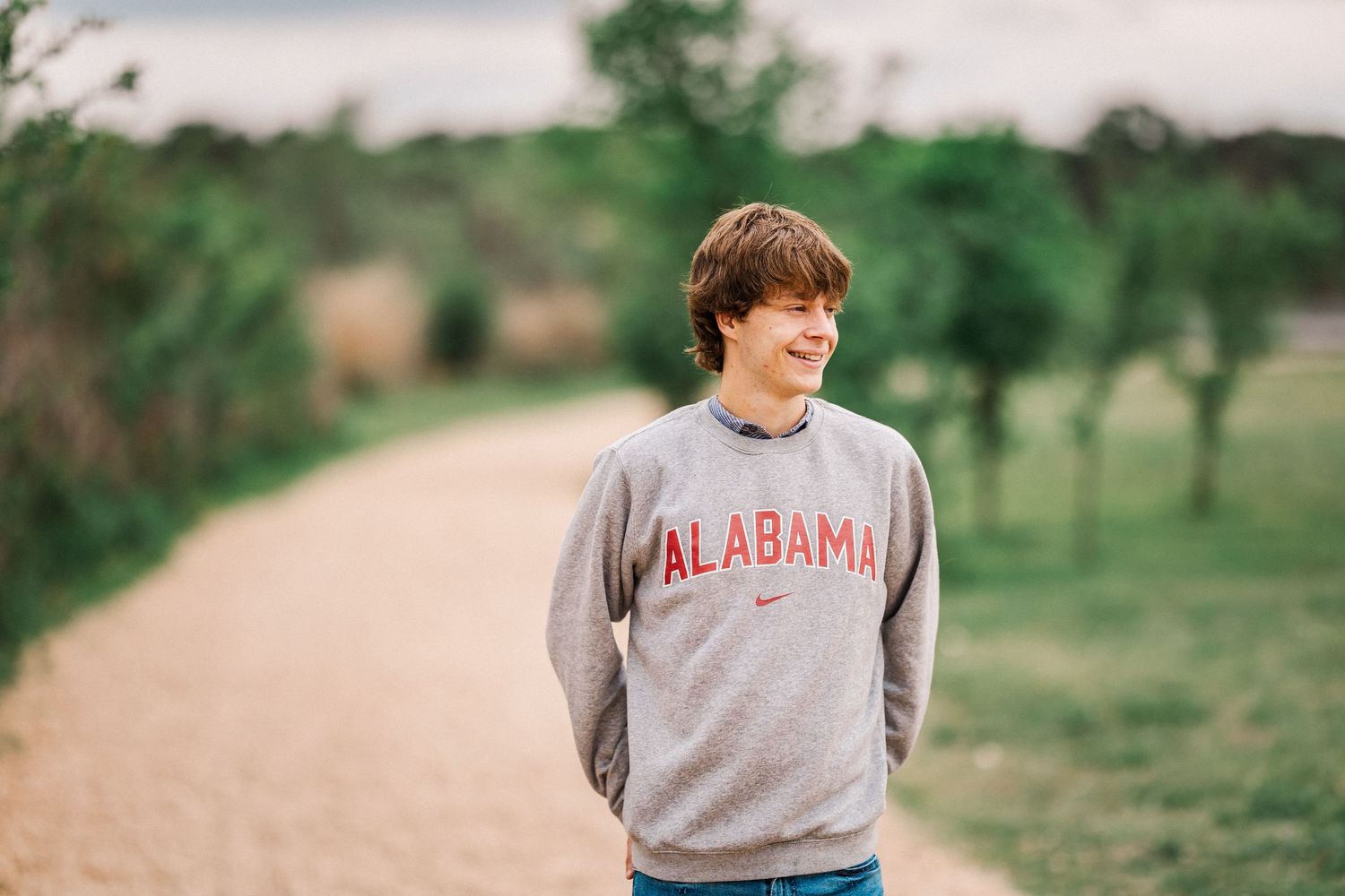 Smiling teen wearing an Alabama Nike sweatshirt standing on a scenic outdoor dirt path.