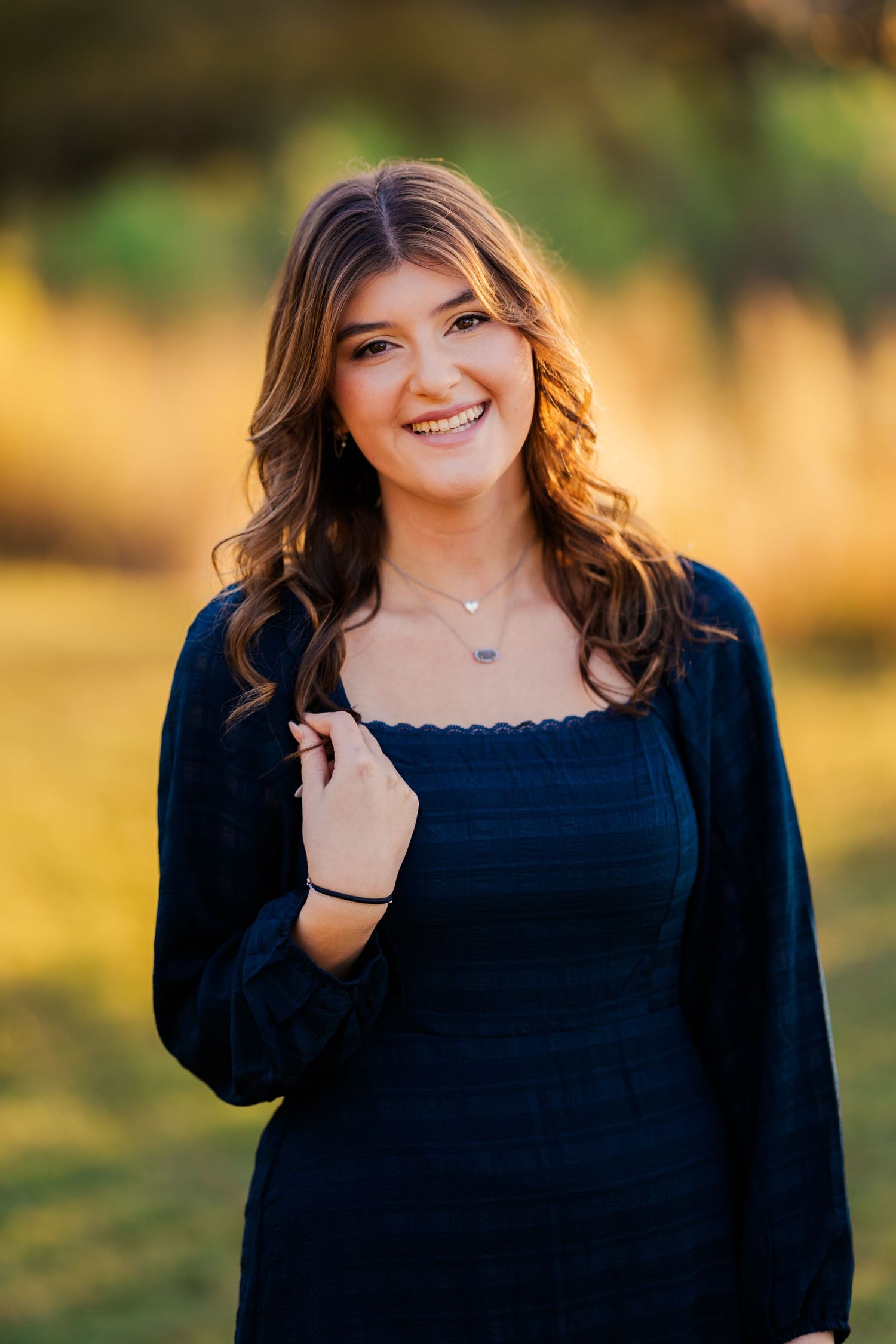 Smiling teenage girl in navy blue dress poses outdoors in golden autumn light at sunset.
