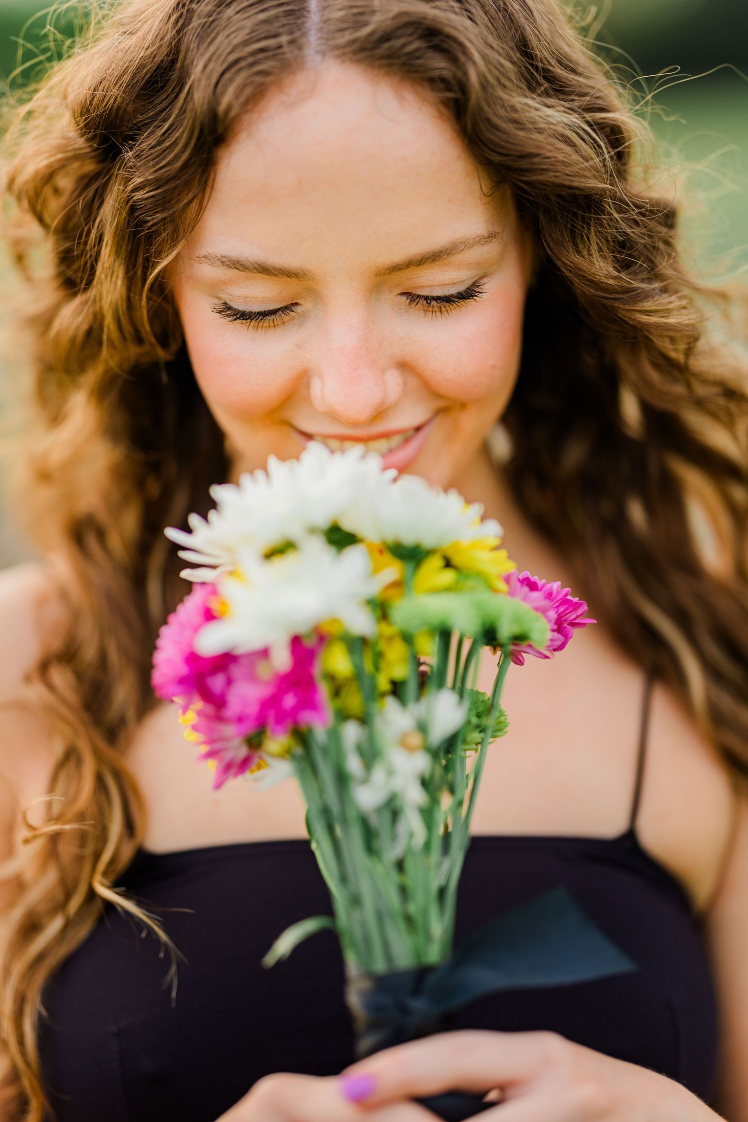 Smiling young woman with curly hair smelling colorful flower bouquet outdoors.