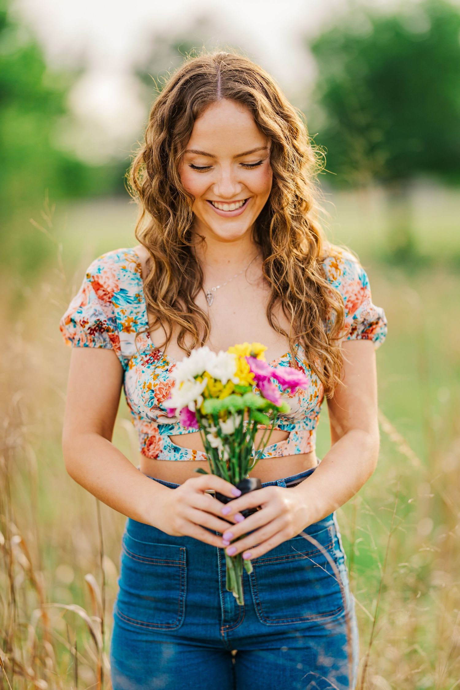 Happy young woman in floral crop top holding colorful bouquet in golden field.