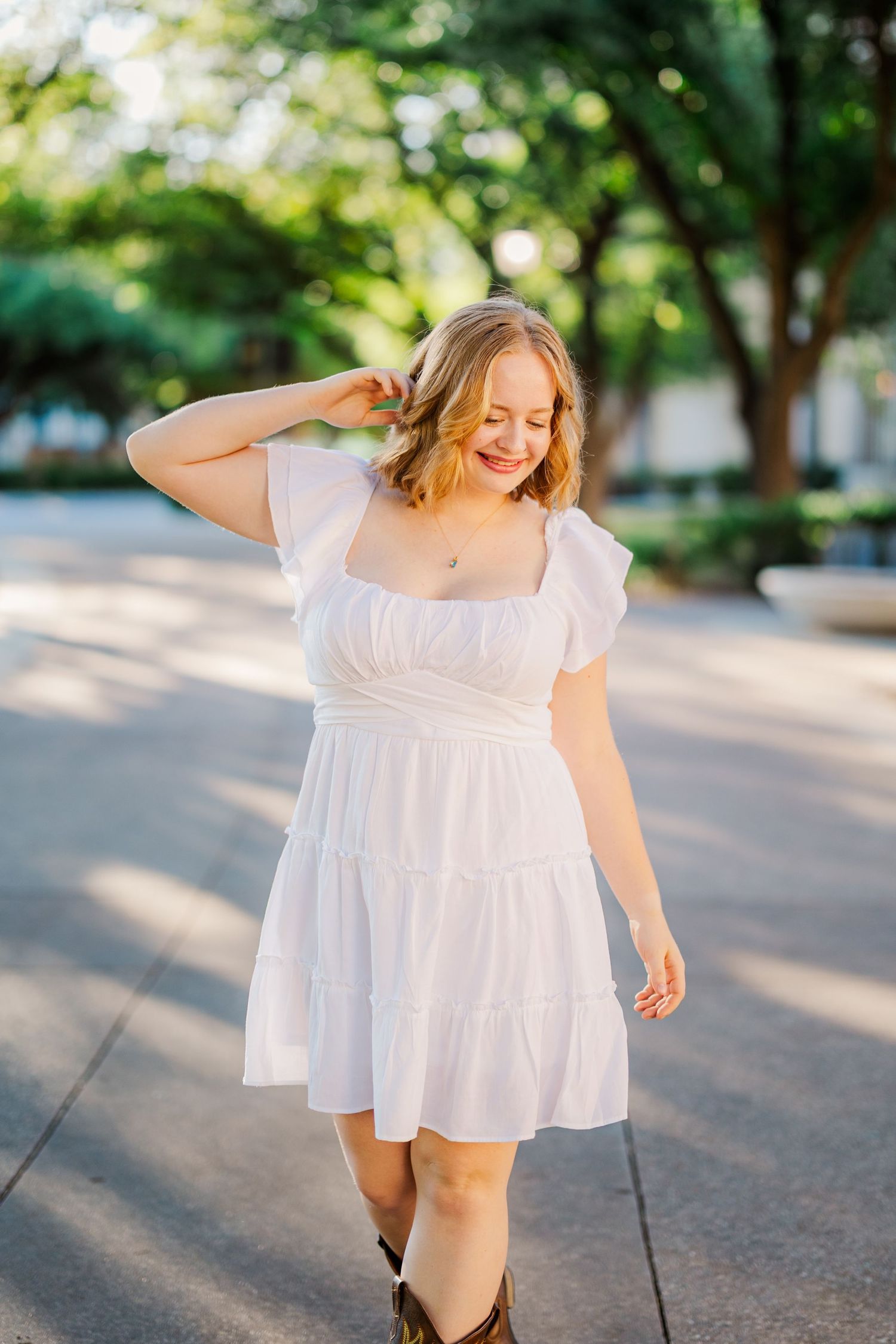 Happy blonde girl in white puff-sleeve dress and cowboy boots walks through a sunny park.