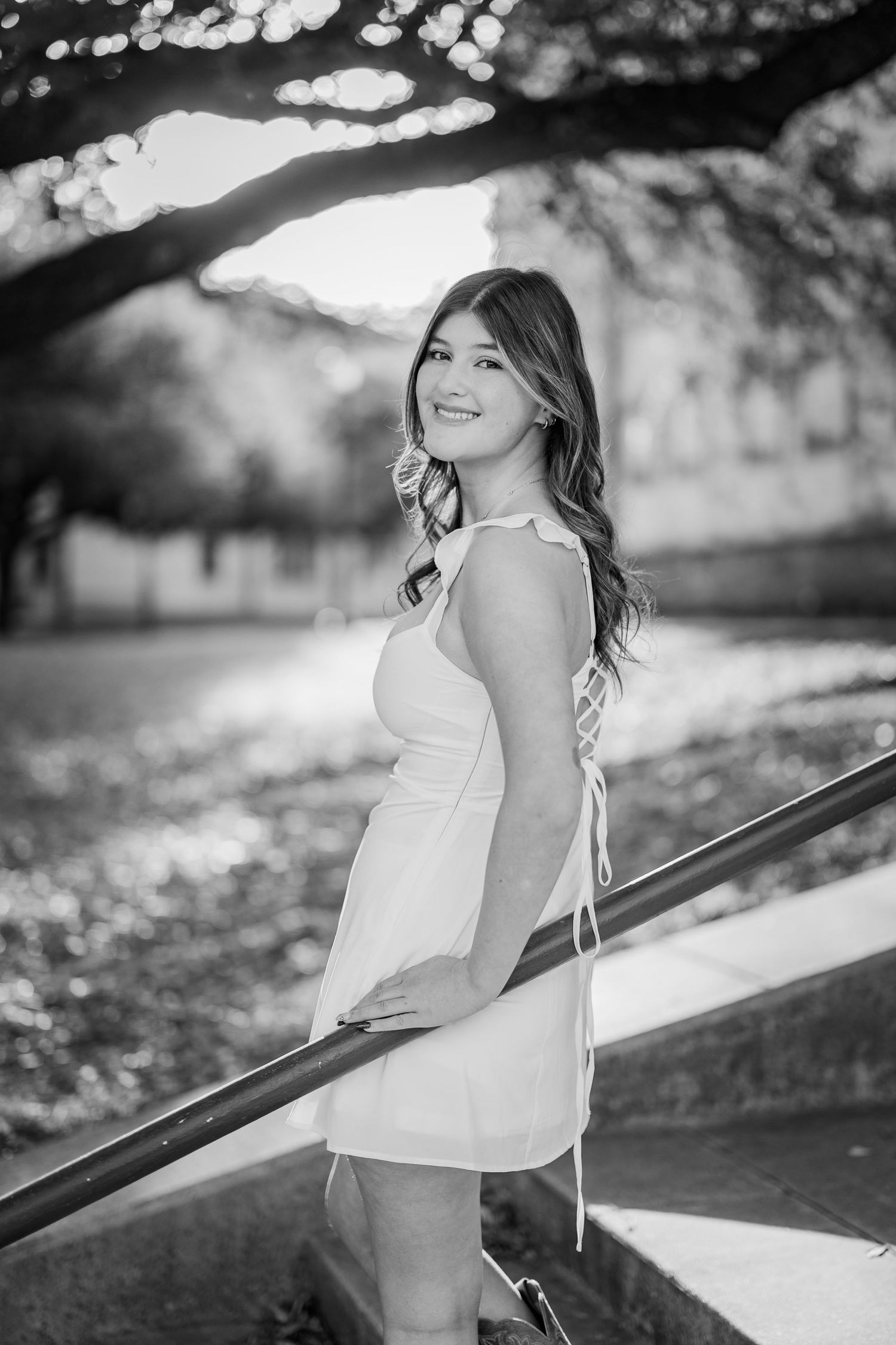 Black and white portrait of smiling teenage girl in white dress on outdoor staircase.