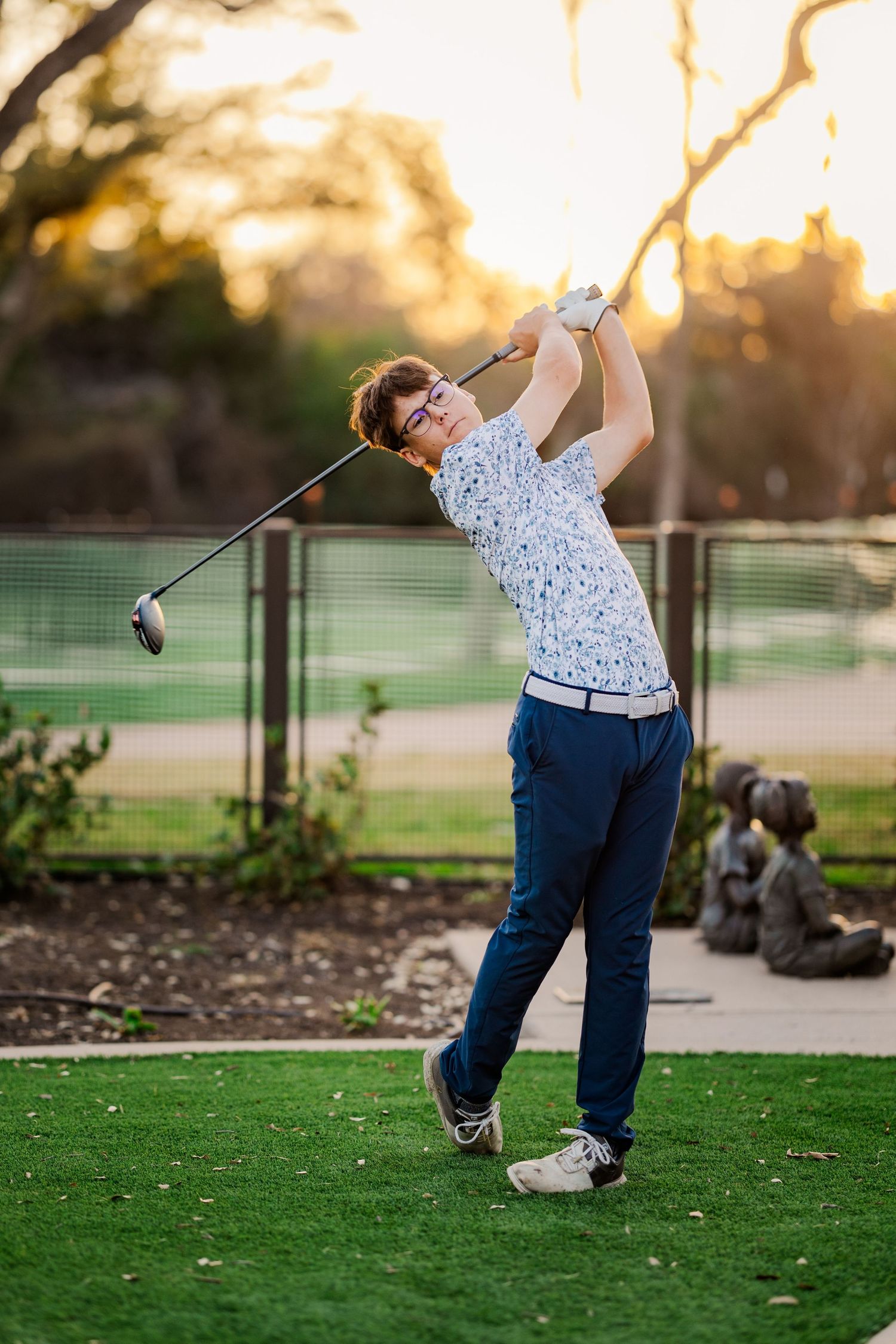 Young male golfer completing a swing on a golf course at golden hour sunset.