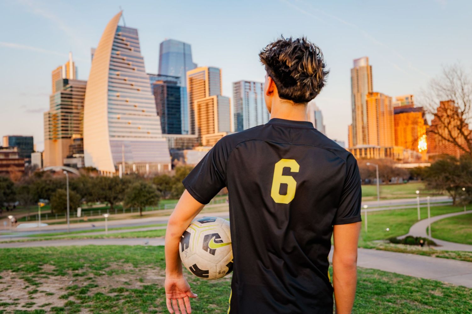 Male soccer player in black number 6 jersey holding ball facing city skyline.