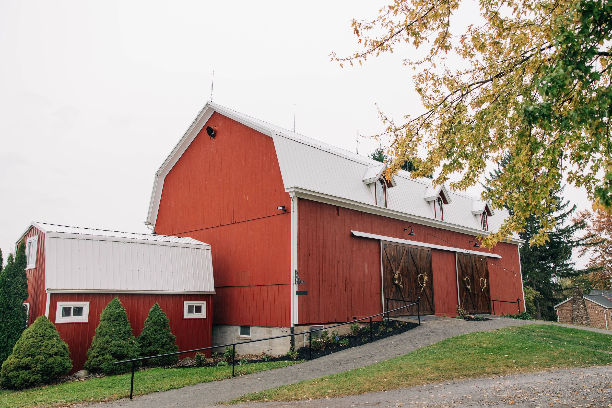 A panoramic view of a large red barn with white trim and multiple buildings on a rural hillside property.