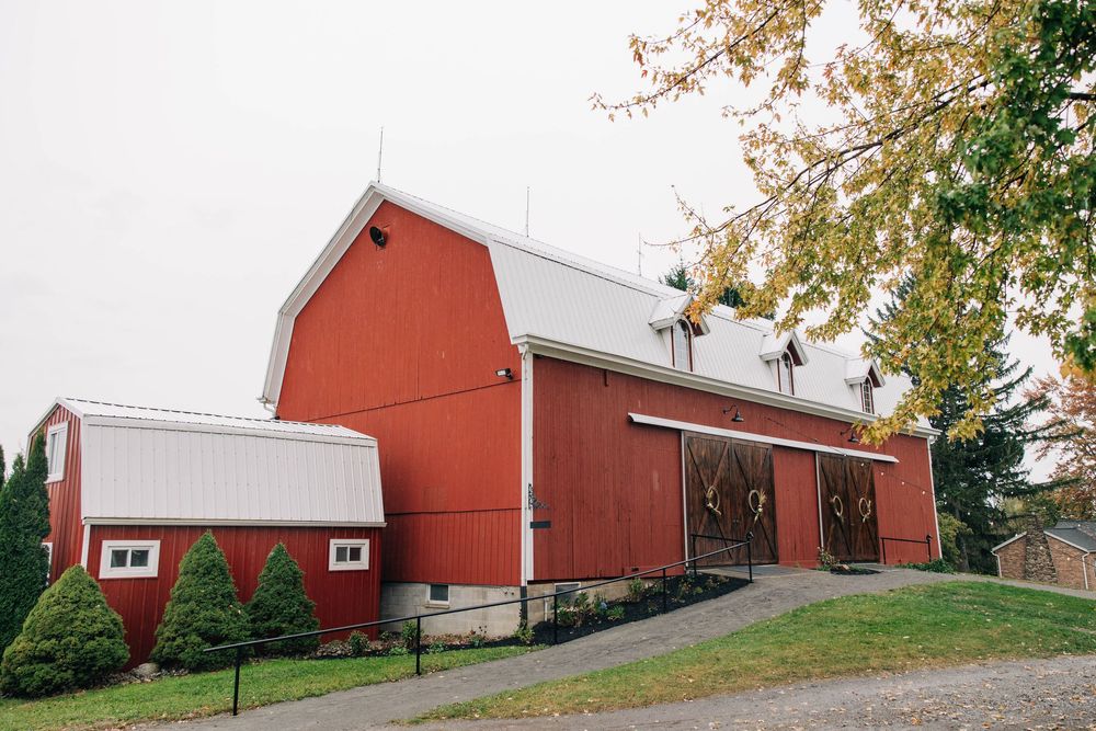 A panoramic view of a large red barn with white trim and multiple buildings on a rural hillside property.