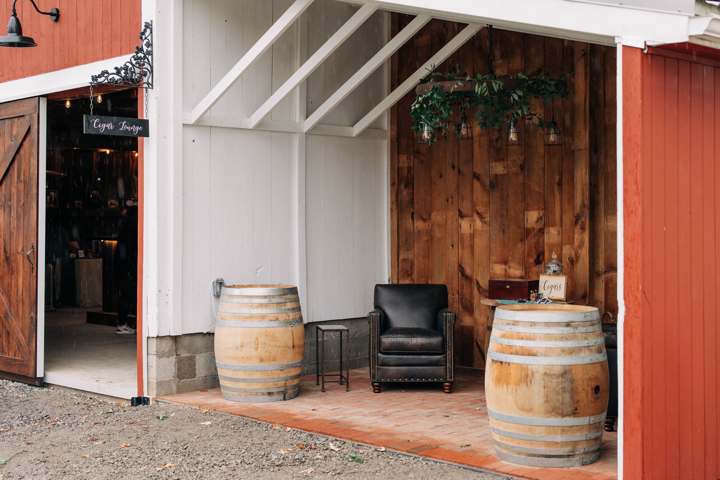 Rustic wooden porch with black leather chair and two wine barrels at a winery tasting room entrance.