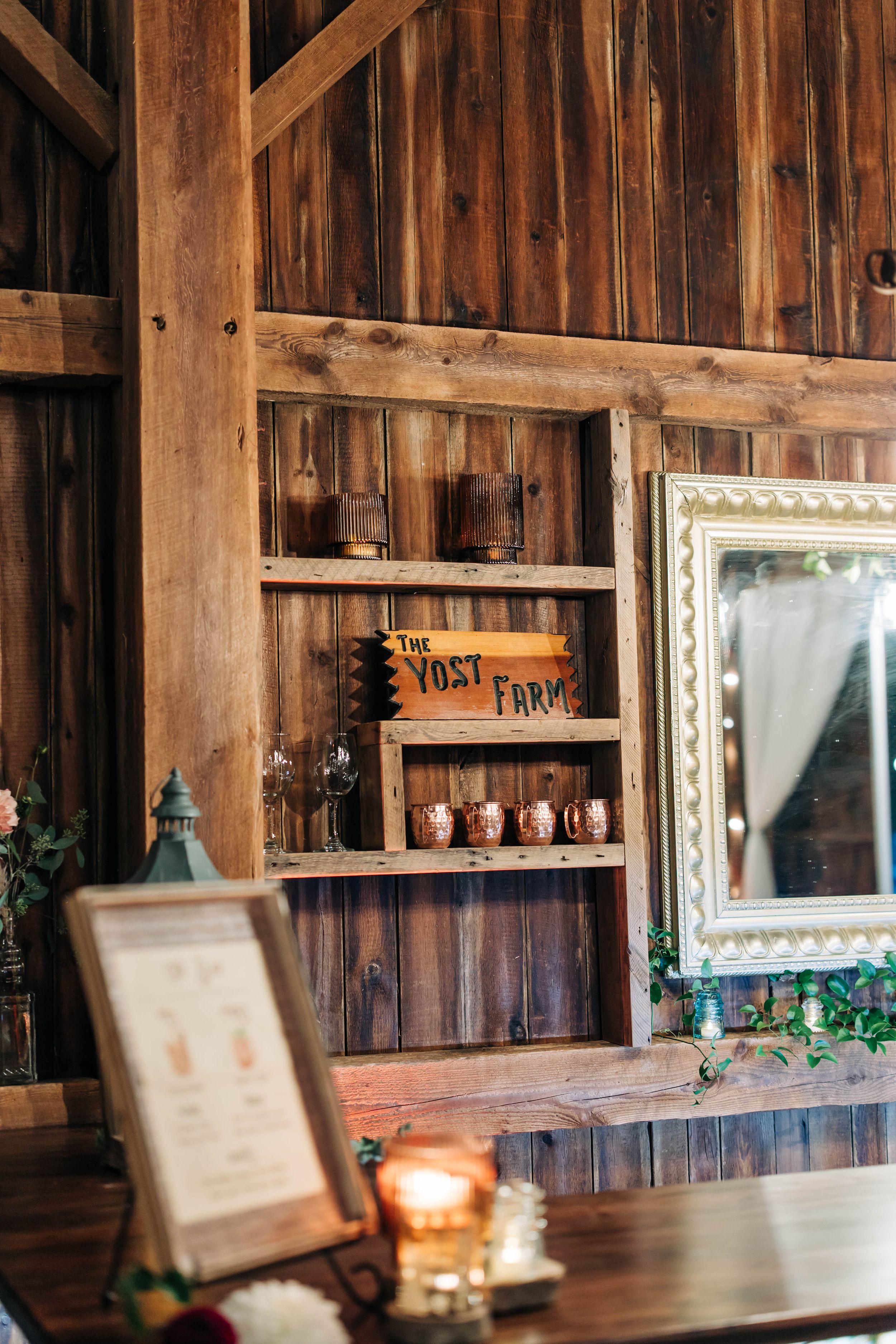 Rustic wooden barn interior with vintage decor, shelving units, and ornate mirror against weathered plank walls.