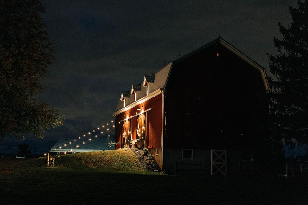 A red barn illuminated at night with string lights creating a warm and romantic atmosphere against a dark sky.