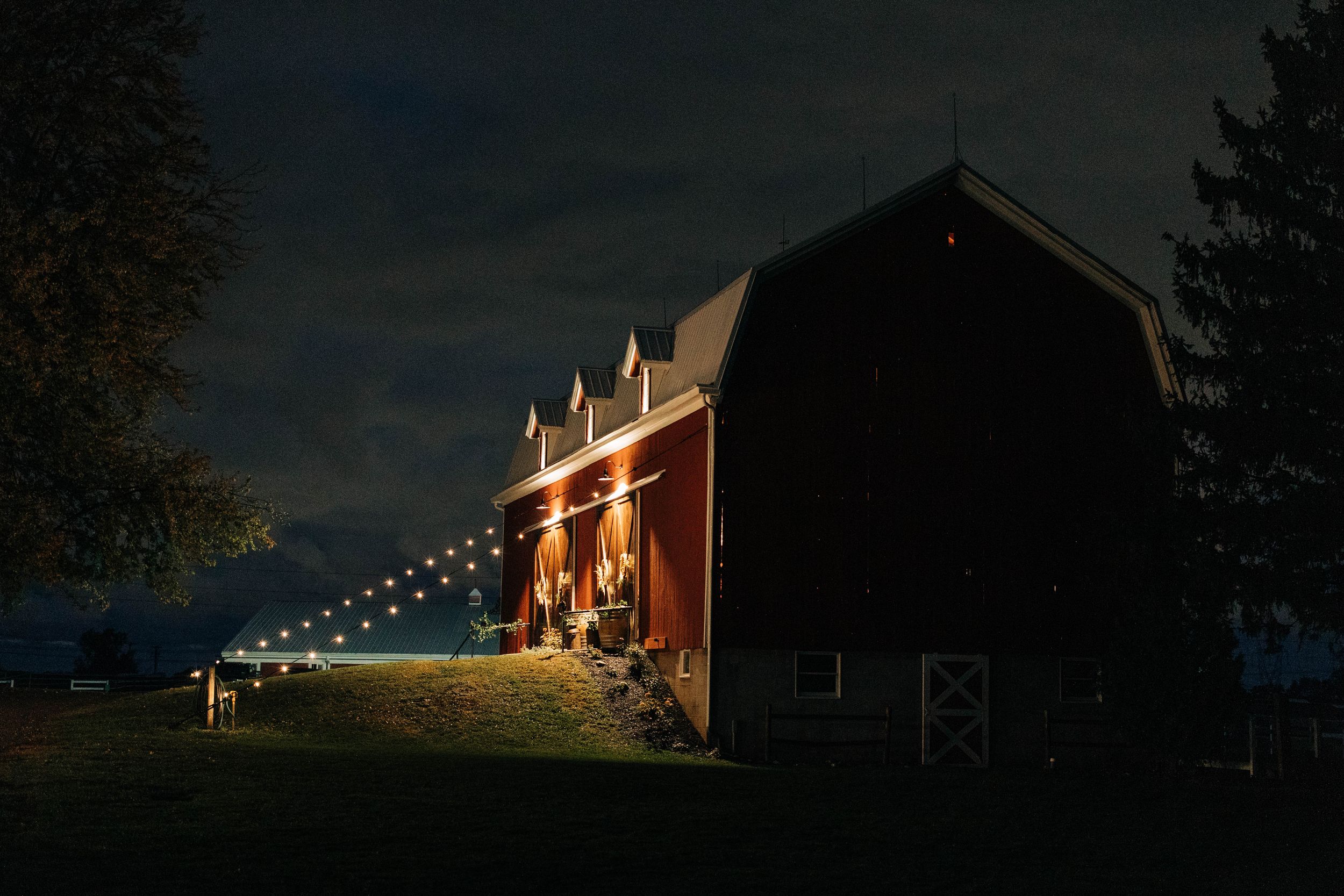 A red barn illuminated at night with string lights creating a warm and romantic atmosphere against a dark sky.