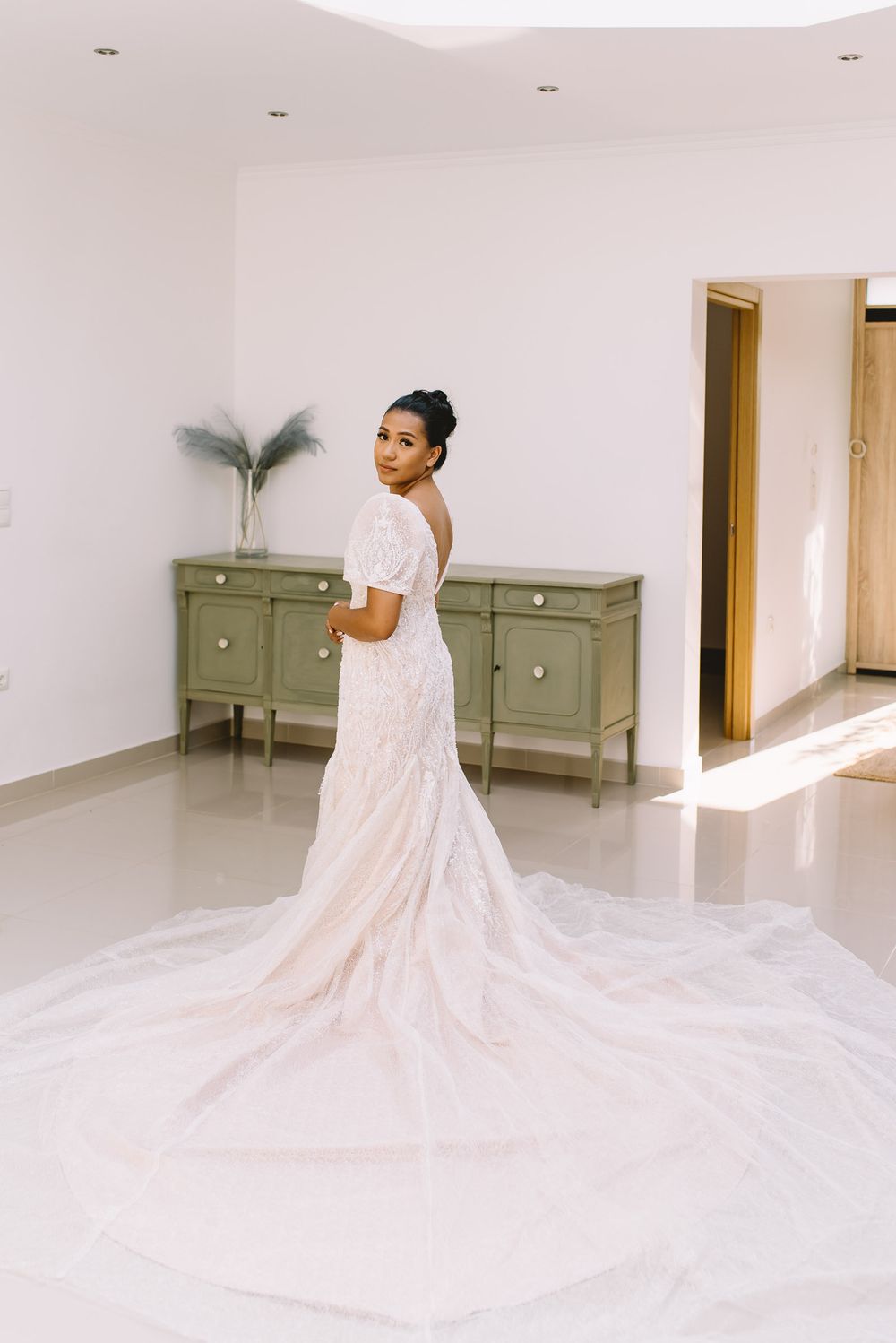 Long flowing cathedral veil trailing across white floor with sage green vintage dressers in background.