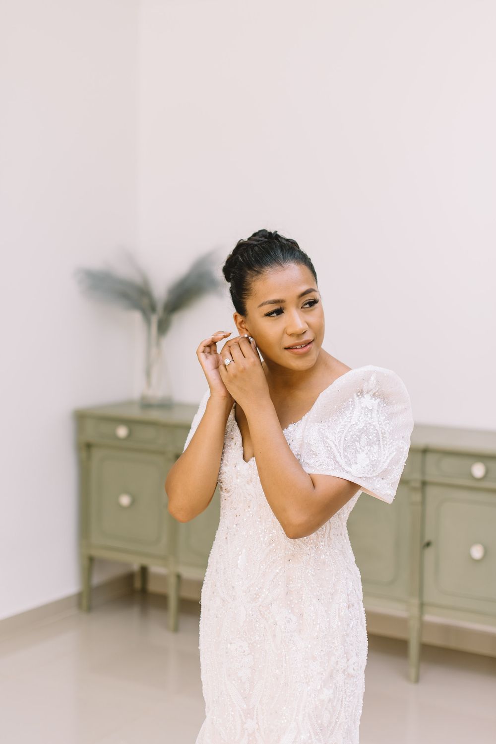 Delicate white lace wedding dress shown in bright minimalist room with sage green furniture.