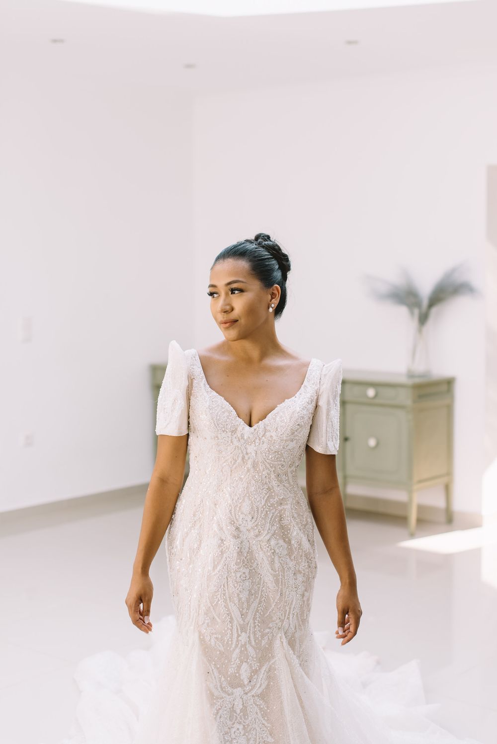 Elegant fitted lace wedding dress with short puff sleeves and sweetheart neckline shown in bright white room.