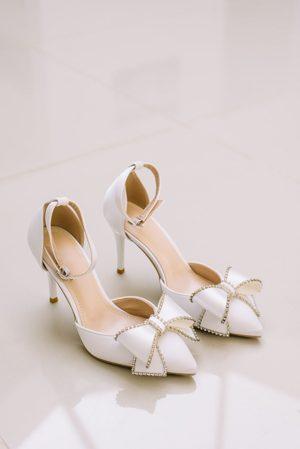 Elegant white bridal shoes with crystal bow details and kitten heels photographed against a light background.