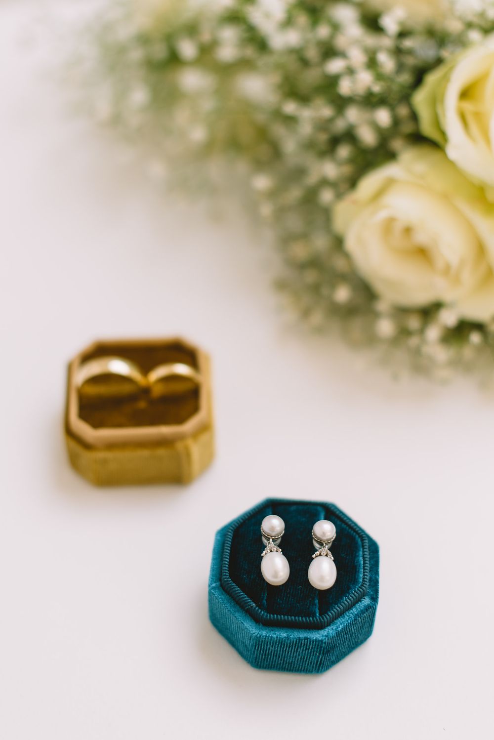 Pearl stud earrings displayed on teal velvet jewelry holders against soft floral background.