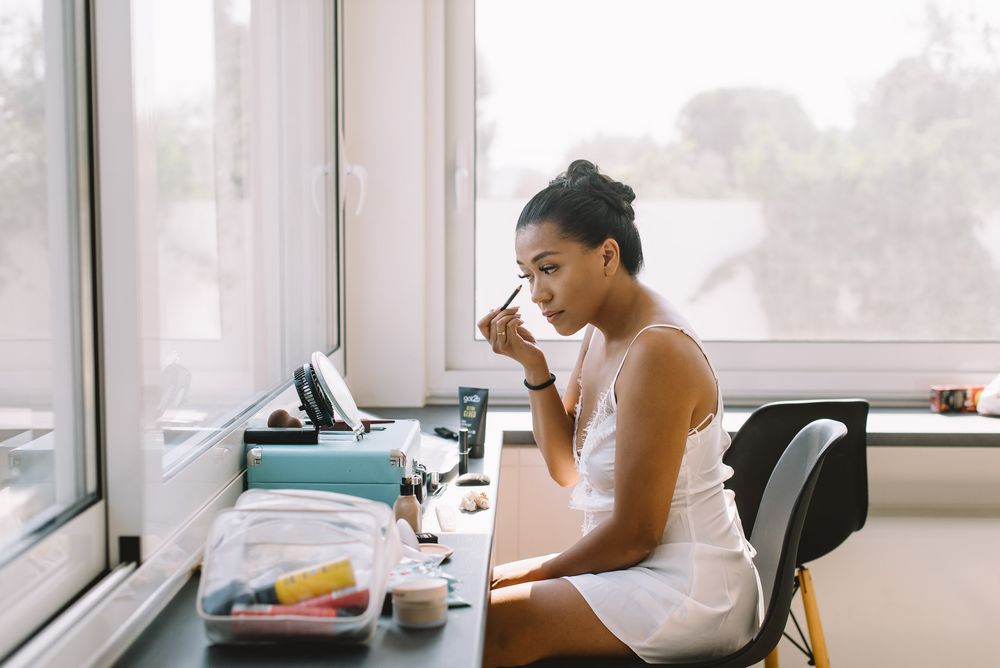 Someone sitting at desk by window wearing tank top, looking stressed while working in home office setting.