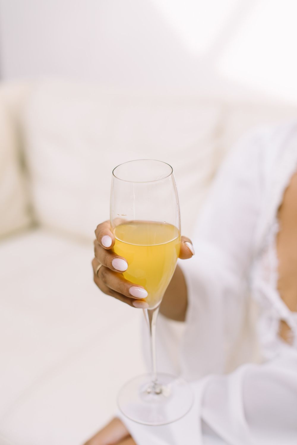Hand holding a champagne glass with golden beverage against a bright white background.