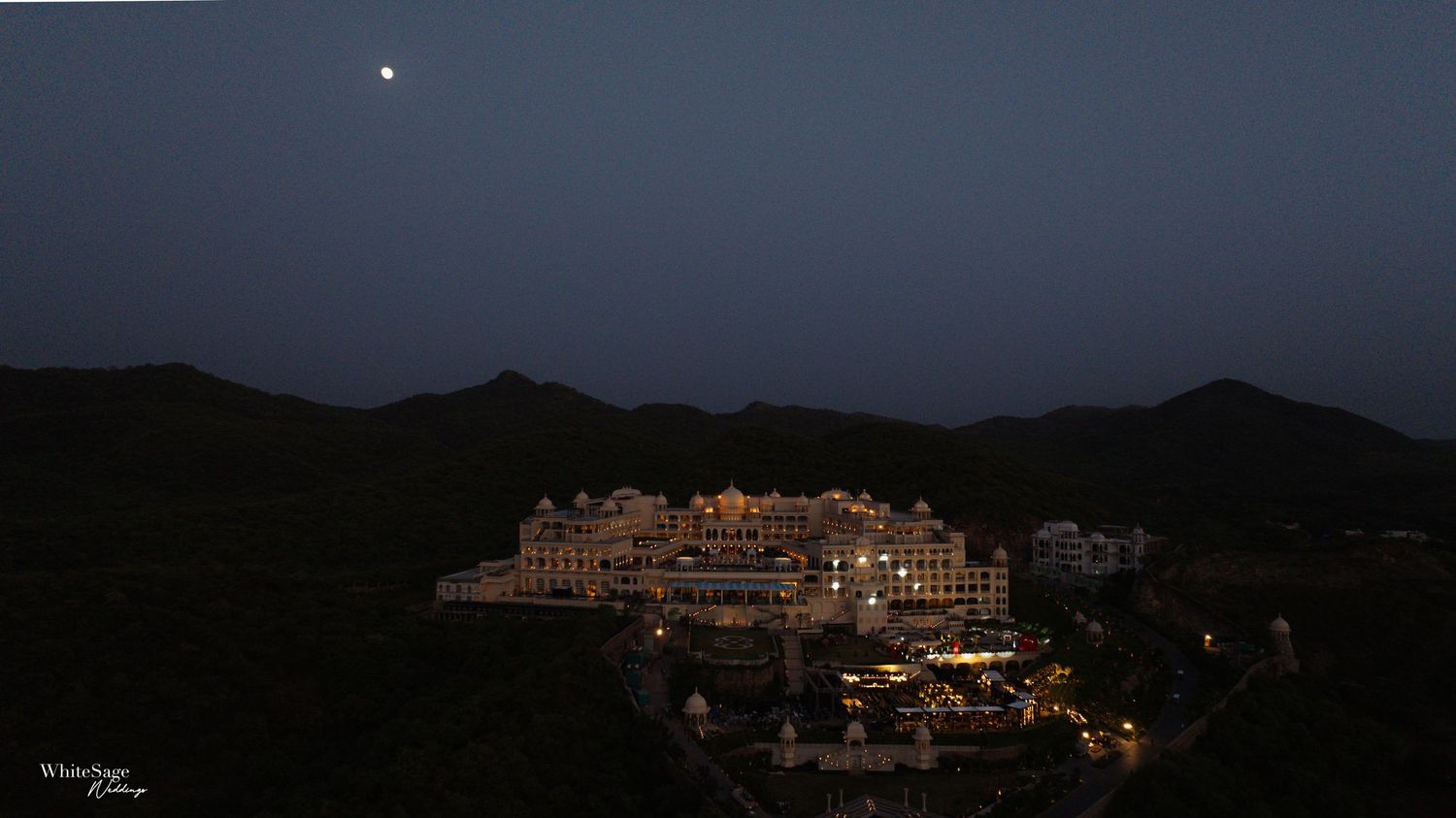 A luxury hotel resort illuminated at twilight against dark mountain silhouettes and night sky.