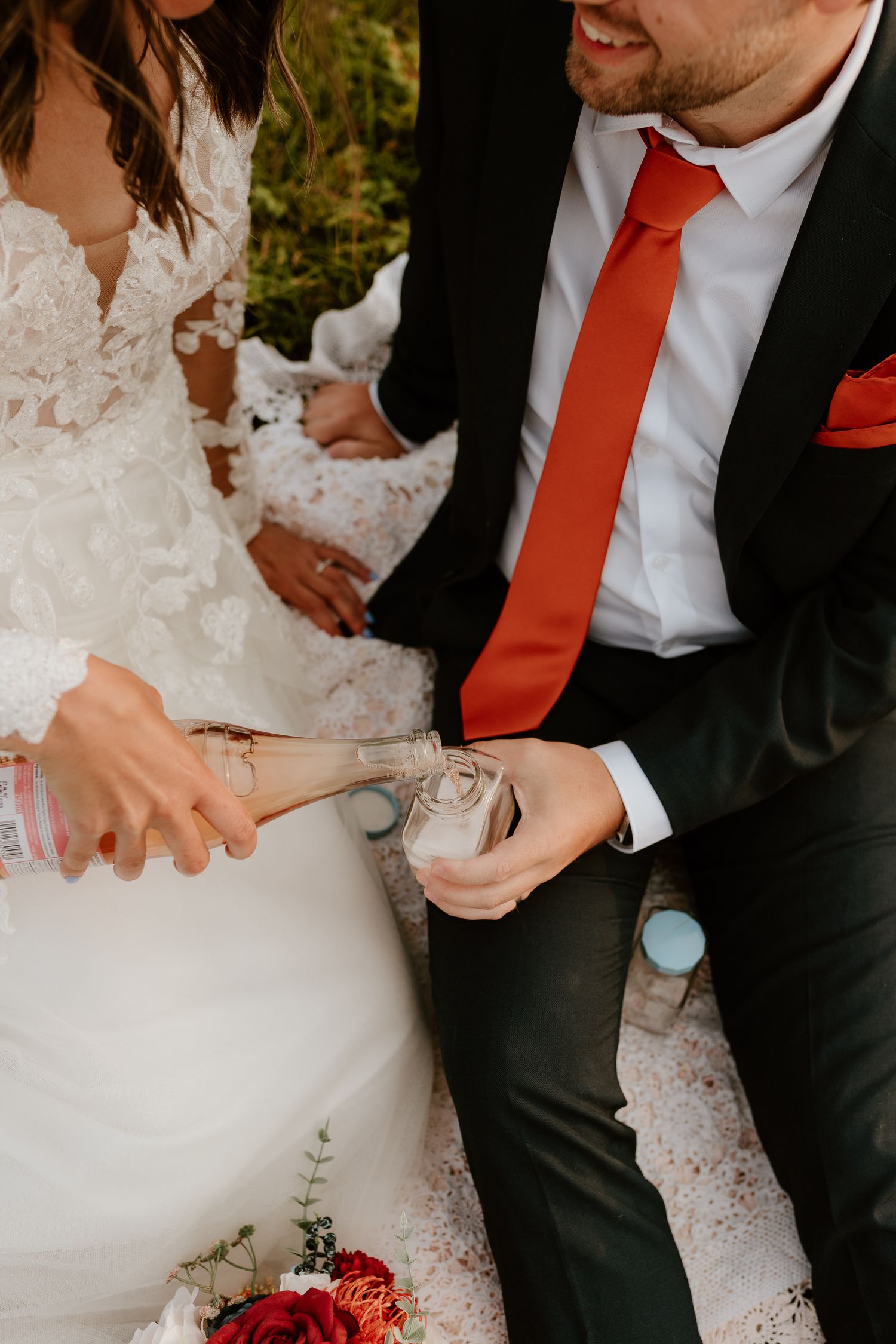 bride and groom sitting on a blanket pouring champagne into their glasses